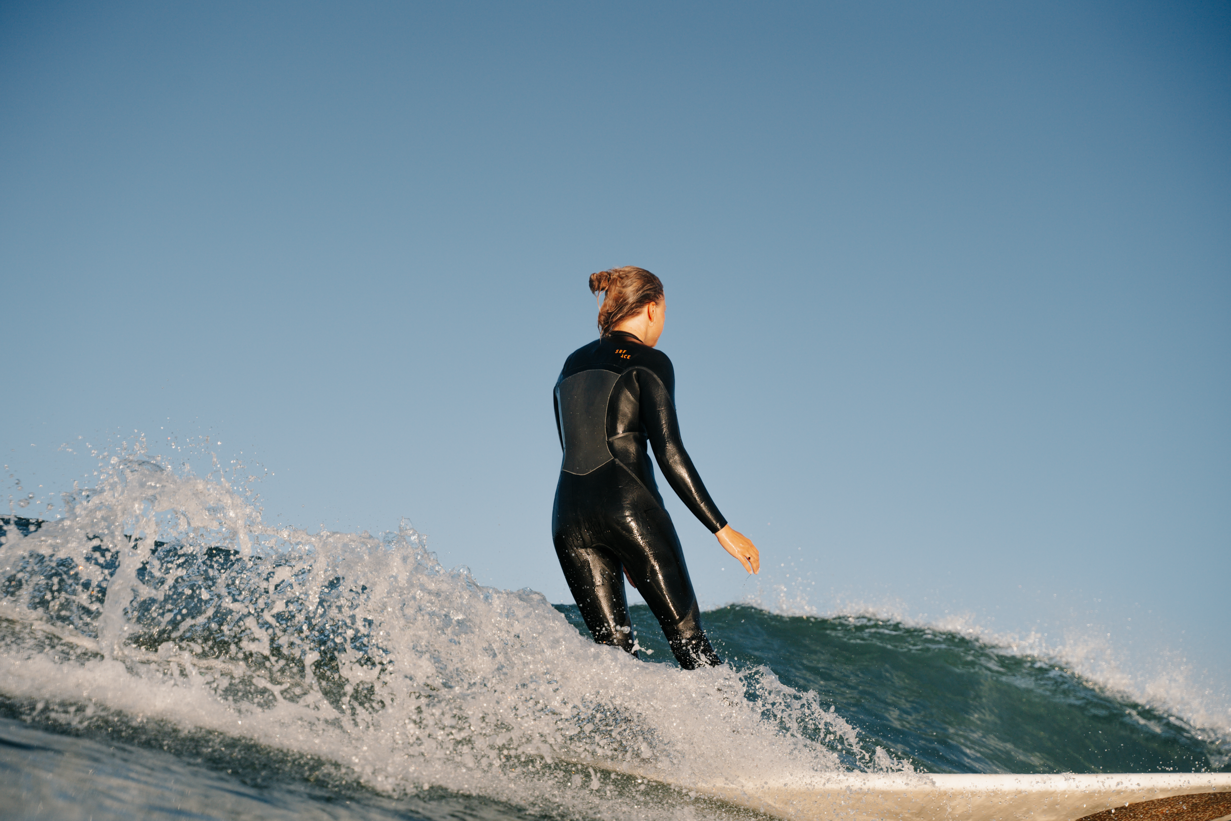 Eine Frau in einem schwarzen Neoprenanzug beim Surfen auf dem Meer