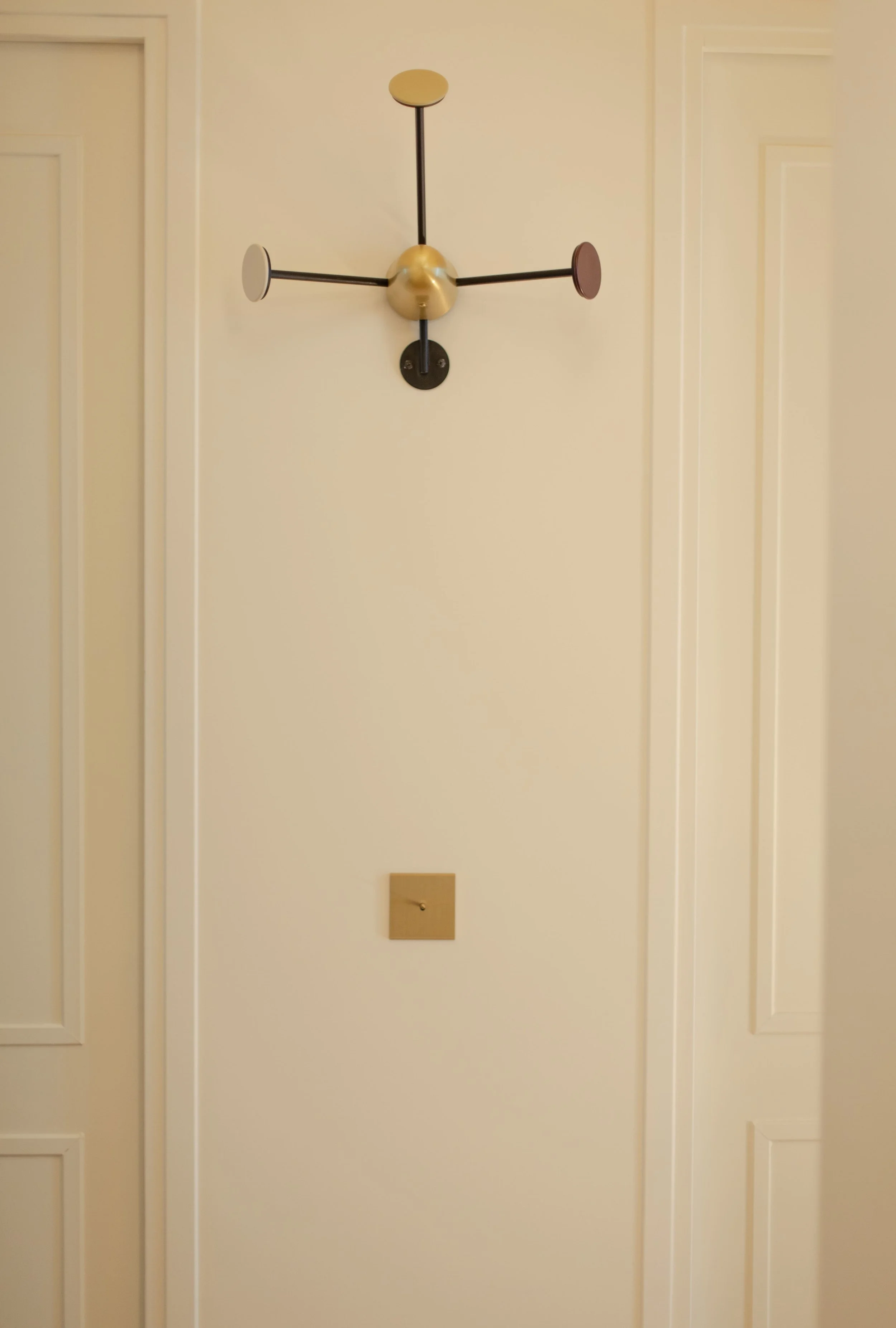 Un mur beige avec un luminaire design moderne au centre, et une prise électrique en dessous, encadré par deux portes blanches