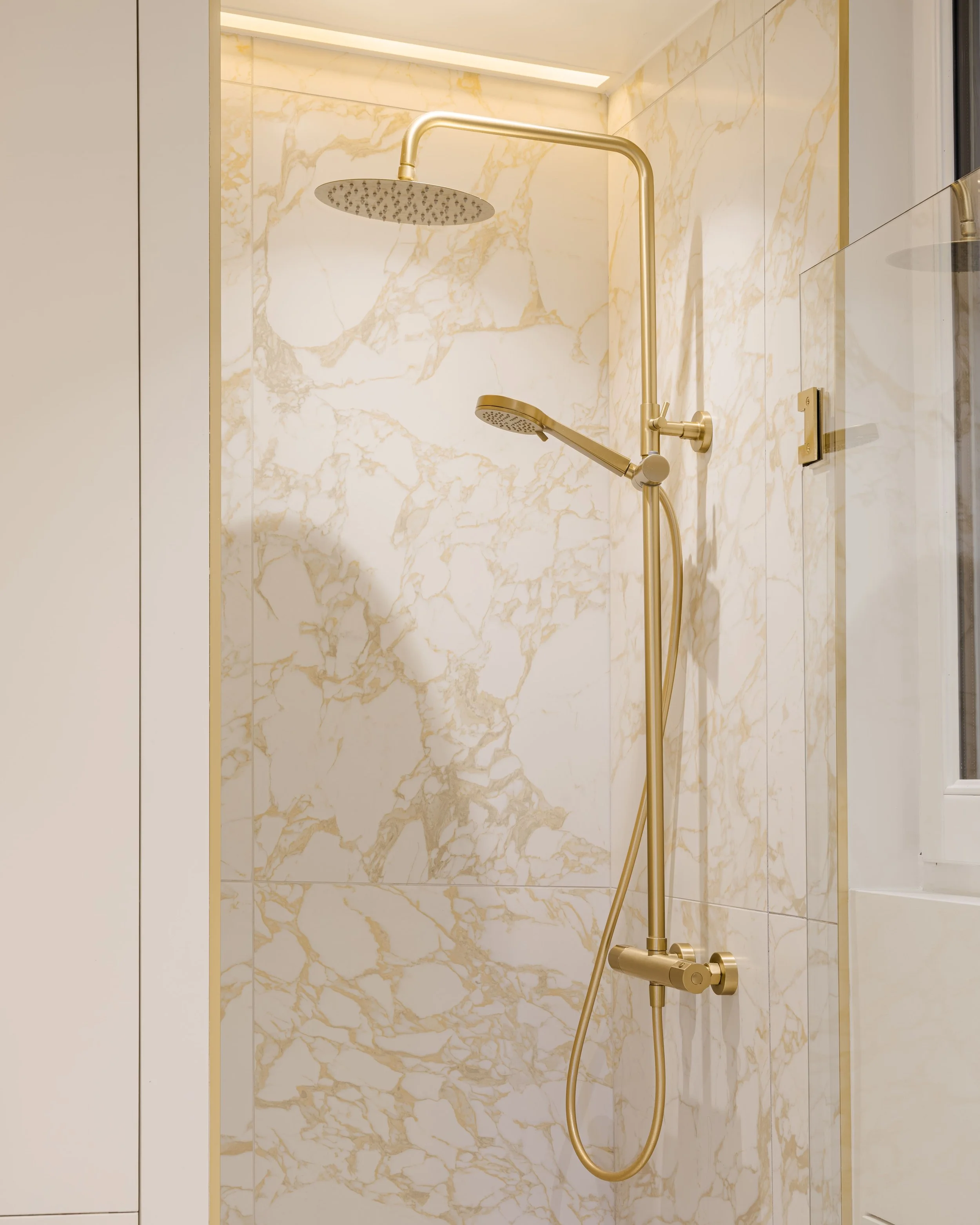 Douchette dans une cabine de douche avec un mur en marbre blanc et ornementé de lignes dorées.