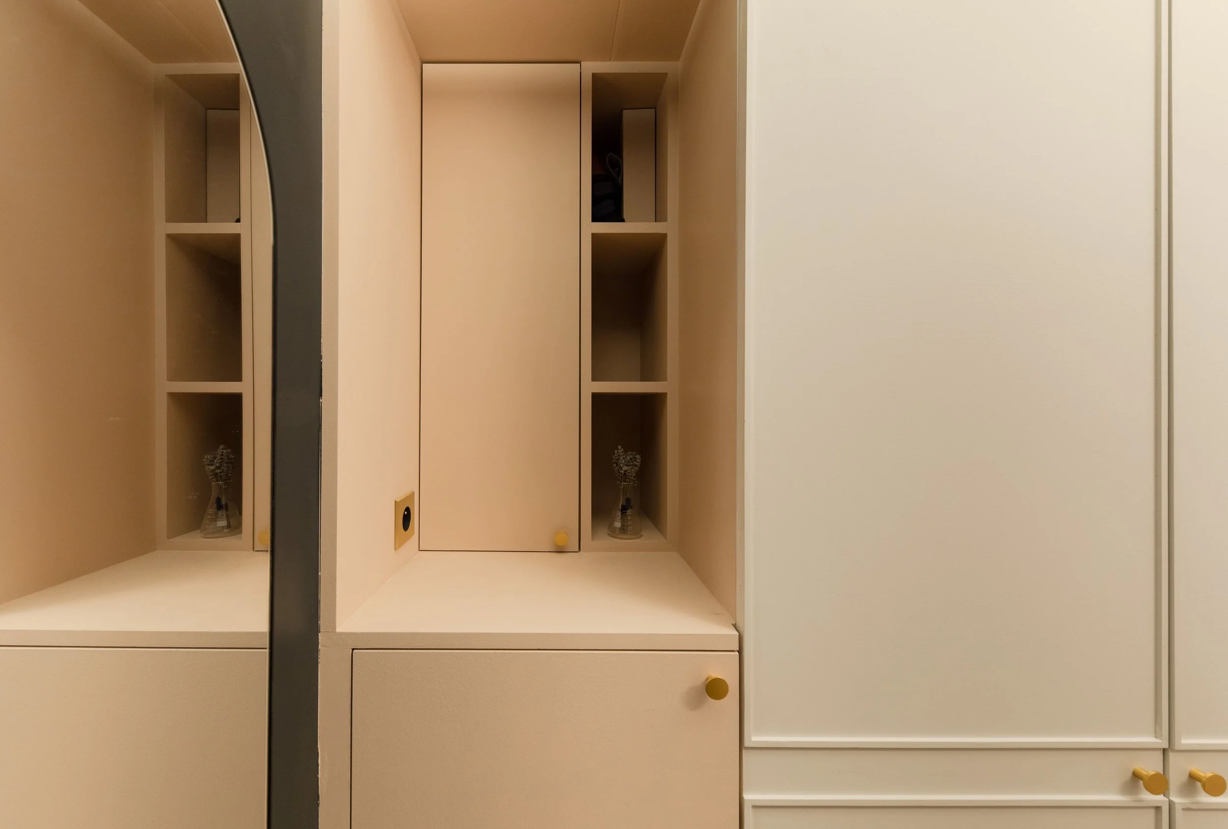 Meuble de rangement moderne blanc avec des étagères ouvertes et des poignées jaunes, contenant des vases avec des fleurs.