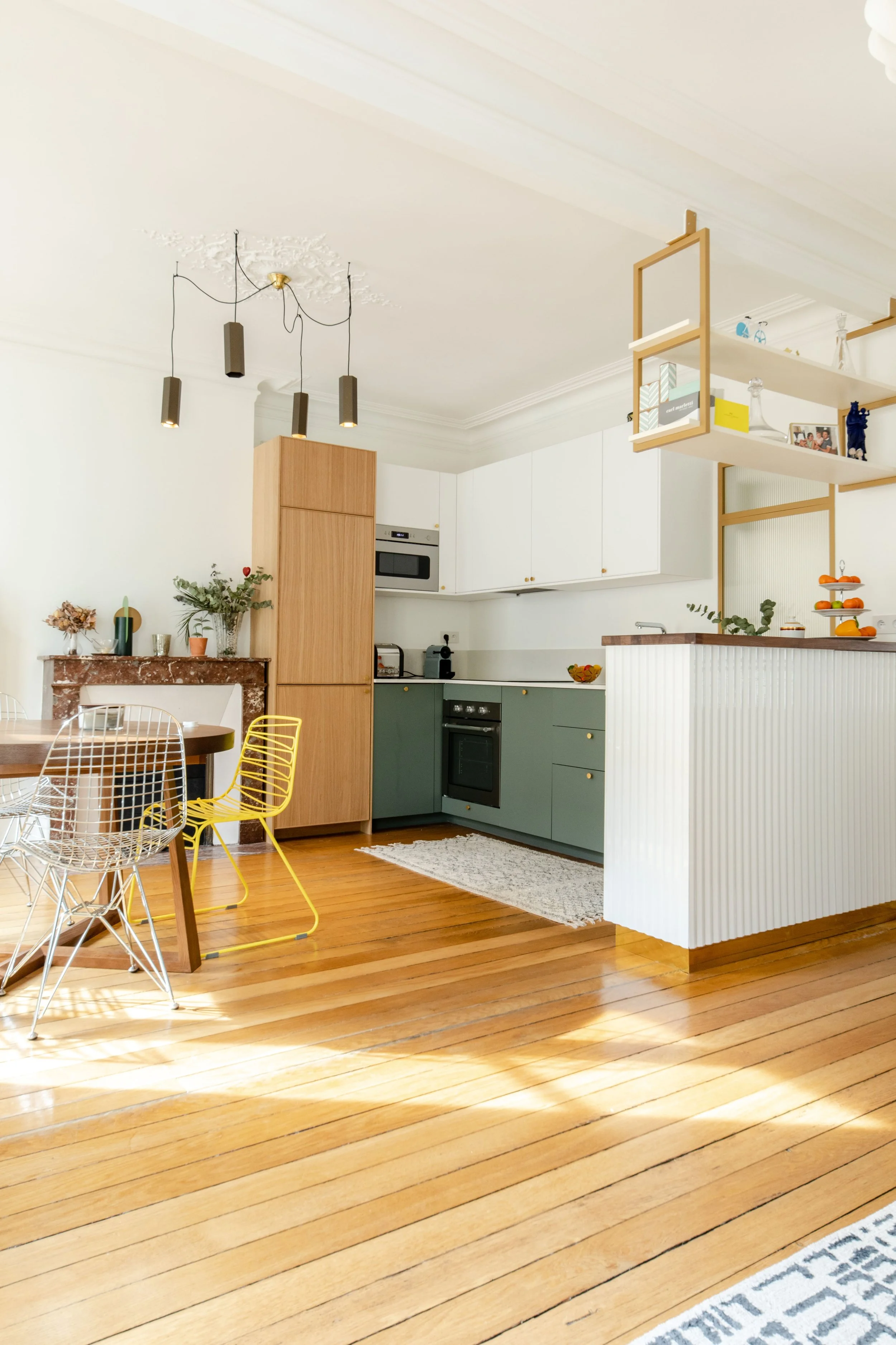 Cuisine moderne avec rayures blanches et vertes, meuble d'époque sur le mur, murs blancs, plan de travail blanc avec une étagère suspendue en bois, plafond blanc avec moulures et lustre noir.