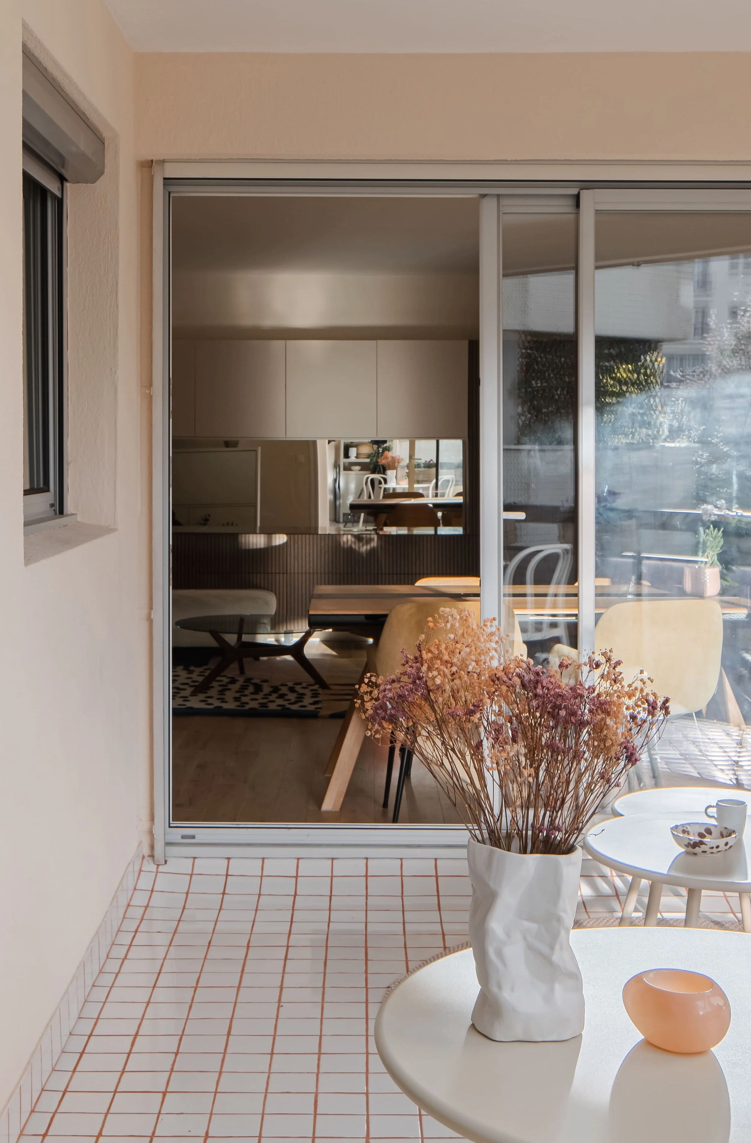 Vue d'une véranda avec des tables, des chaises et un vase de fleurs séchées.