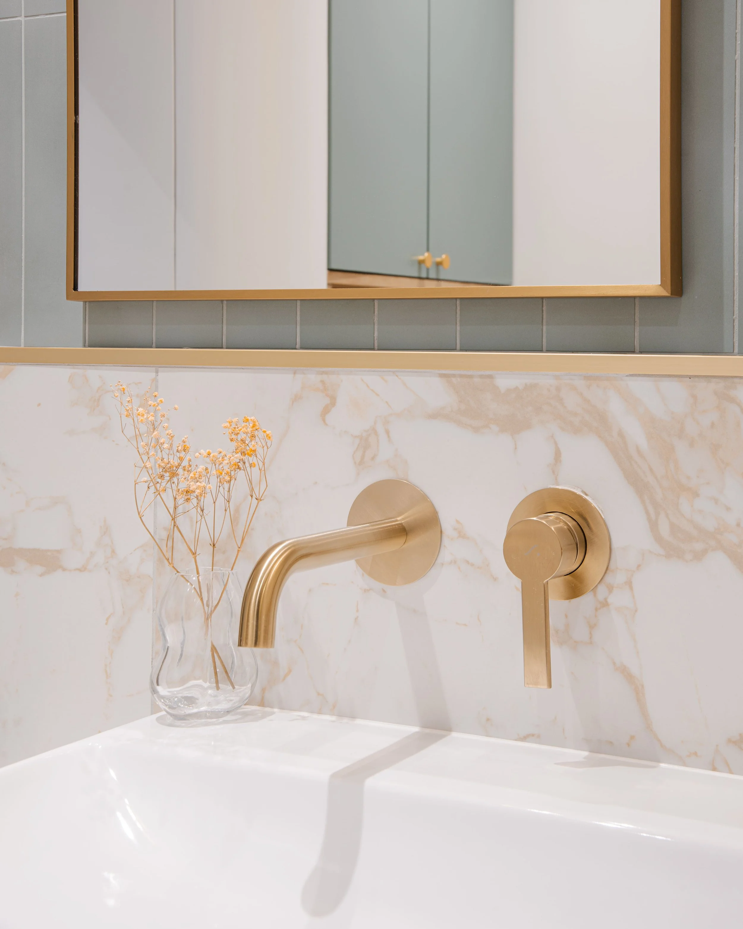 Lavabo avec un distributeur de savon, une vasque en marbre, un miroir et un vase avec des fleurs séchées dans une salle de bain moderne