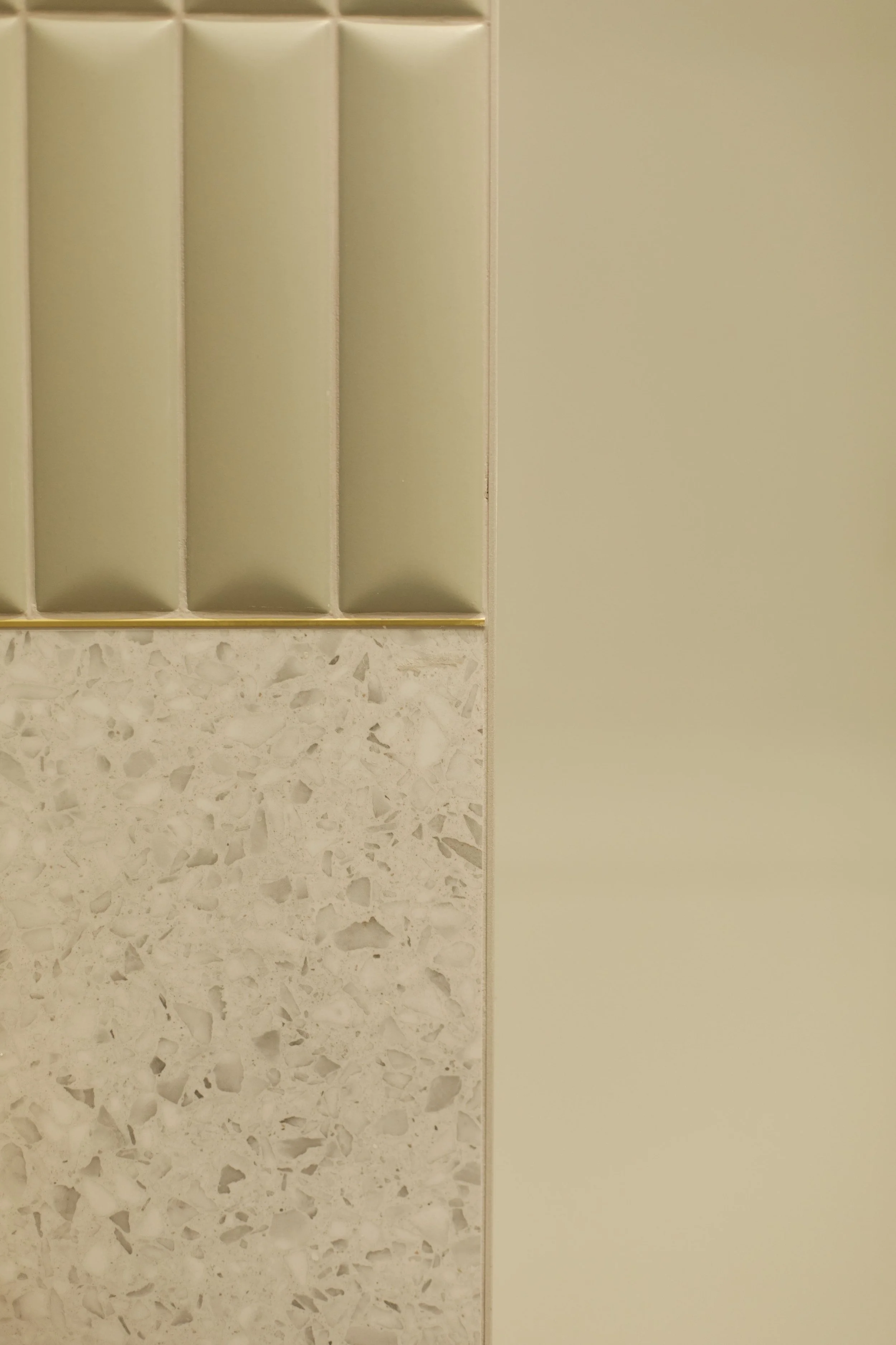 Détail d'une surface en céramique beige avec un motif de terrazzo et une section de carreaux en relief vert mousse.