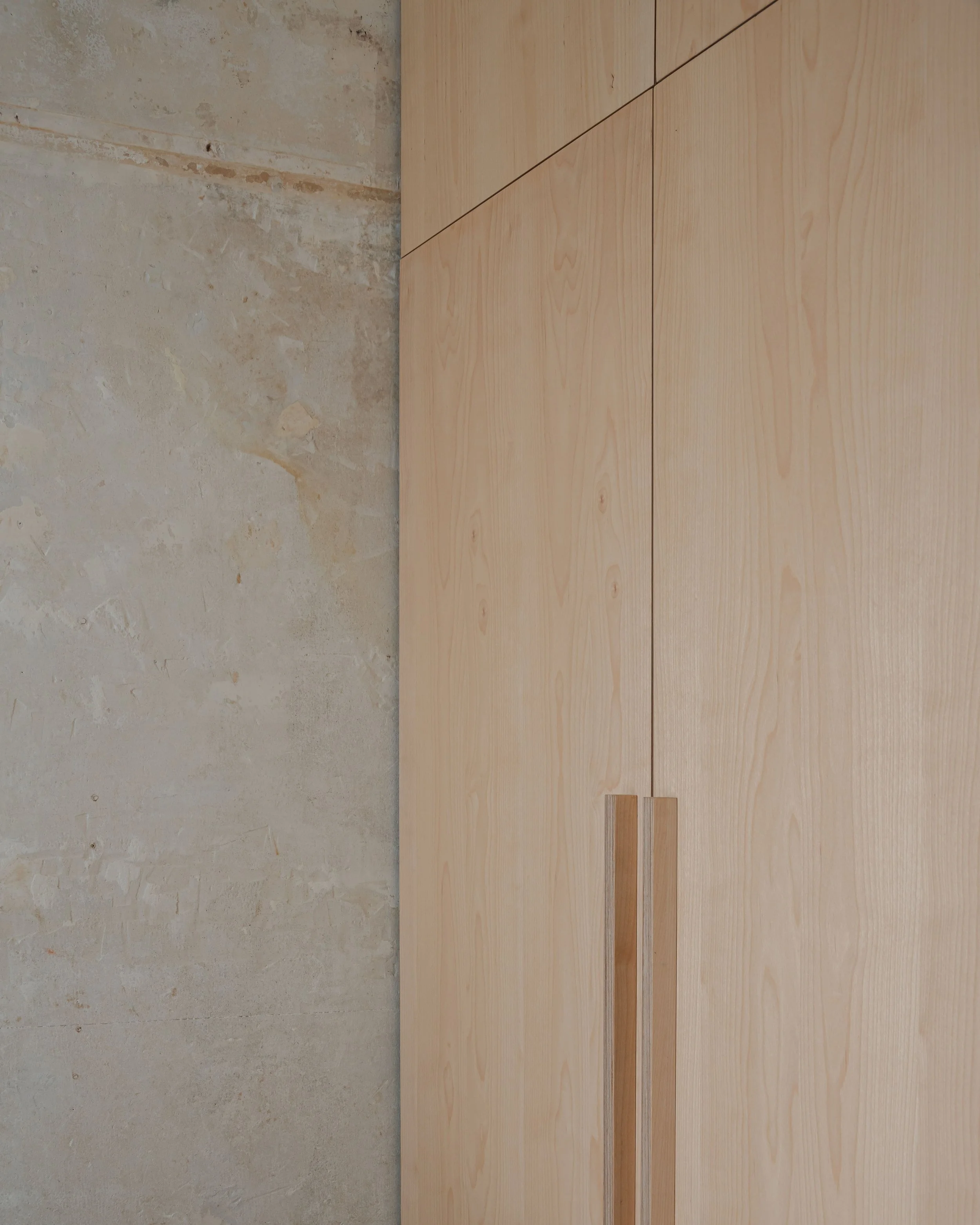 Armoires en bois clair dans une pièce avec un mur en béton brut.