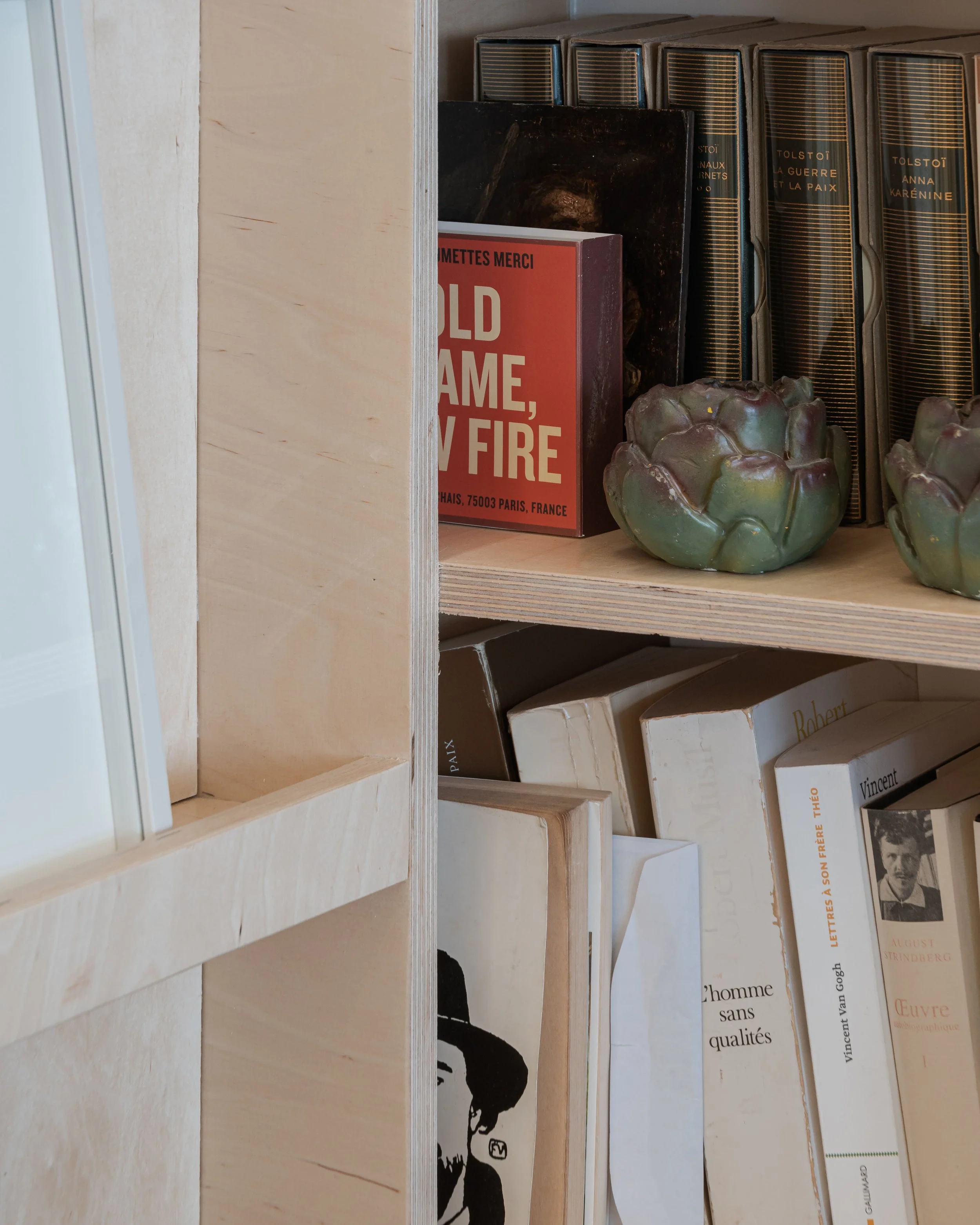 Une étagère en bois contenant plusieurs livres, deux céramiques de couleur verte, et un livre rouge intitulé 'Old Flame, My Fire'.
