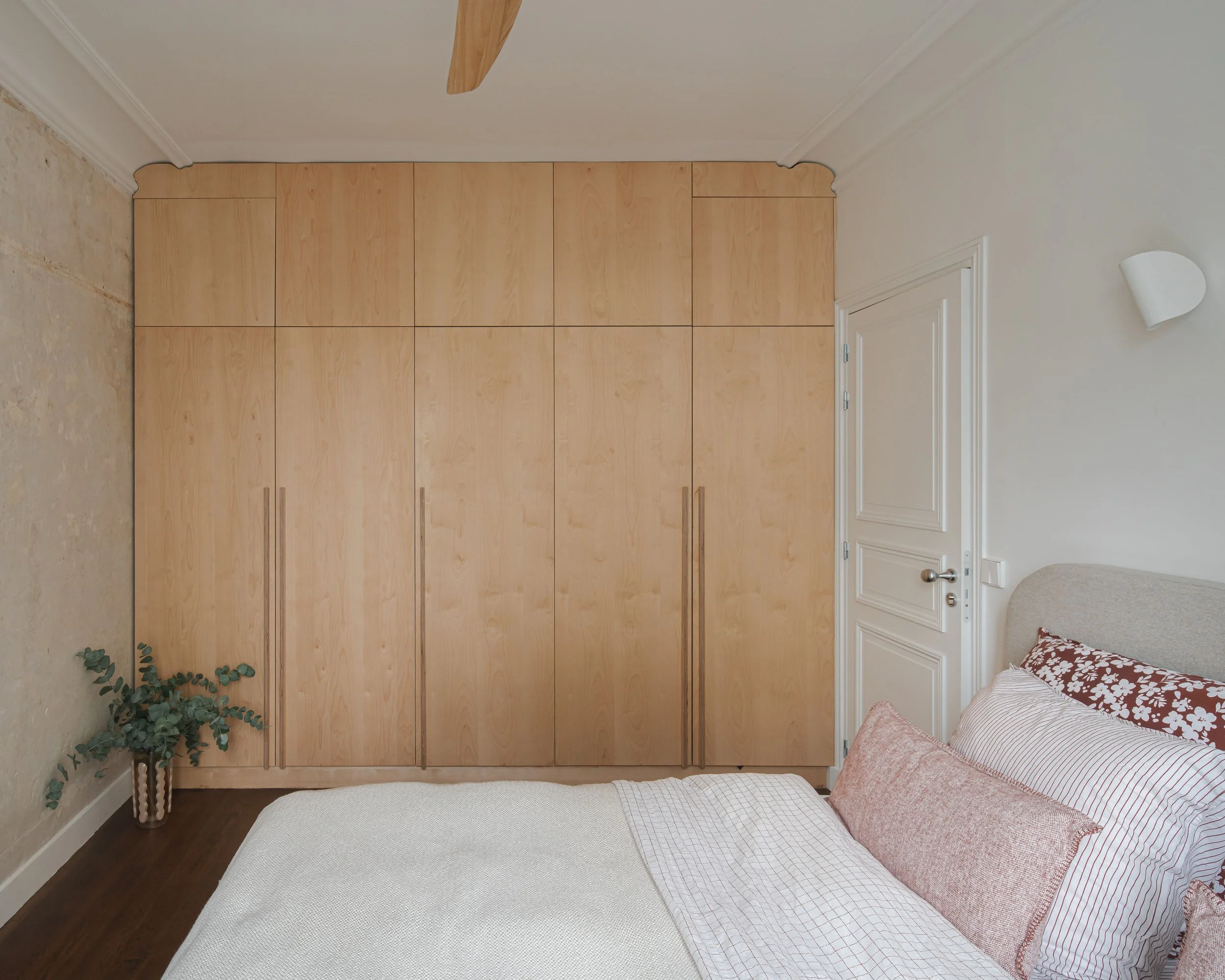 Chambre à coucher avec un lit, une armoire en bois clair, une porte blanche et un mur blanc, décoration simple et épurée.