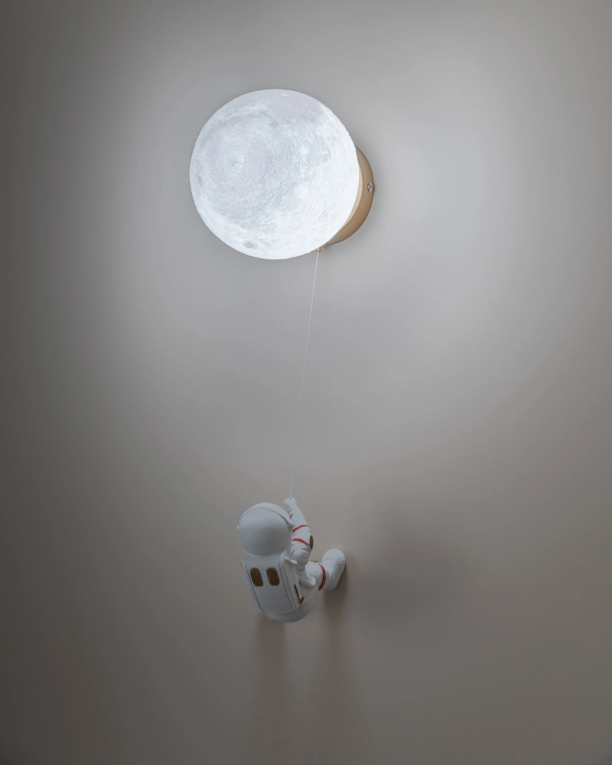 Lampe de chevet avec un design de lune et un petit astronaute suspendu par une ficelle.