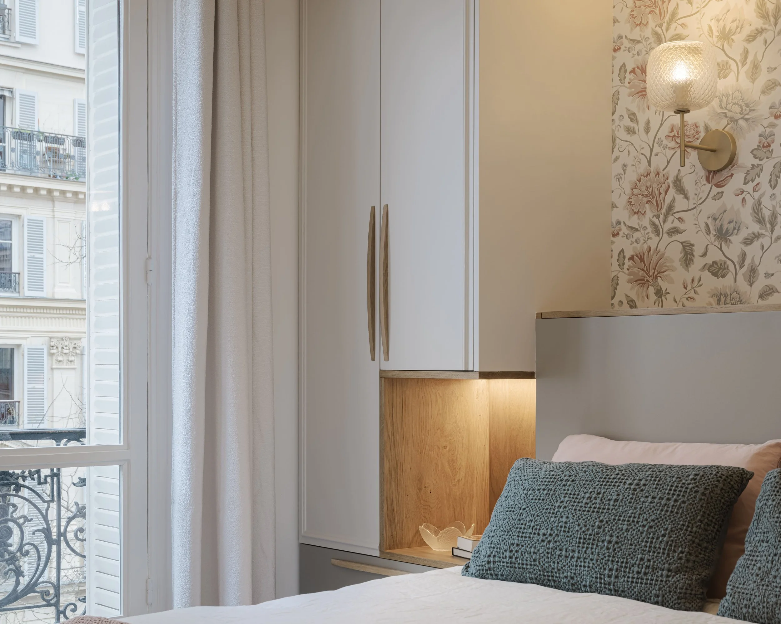Chambre avec lit, oreillers gris, mur à motifs floraux, lampe murale