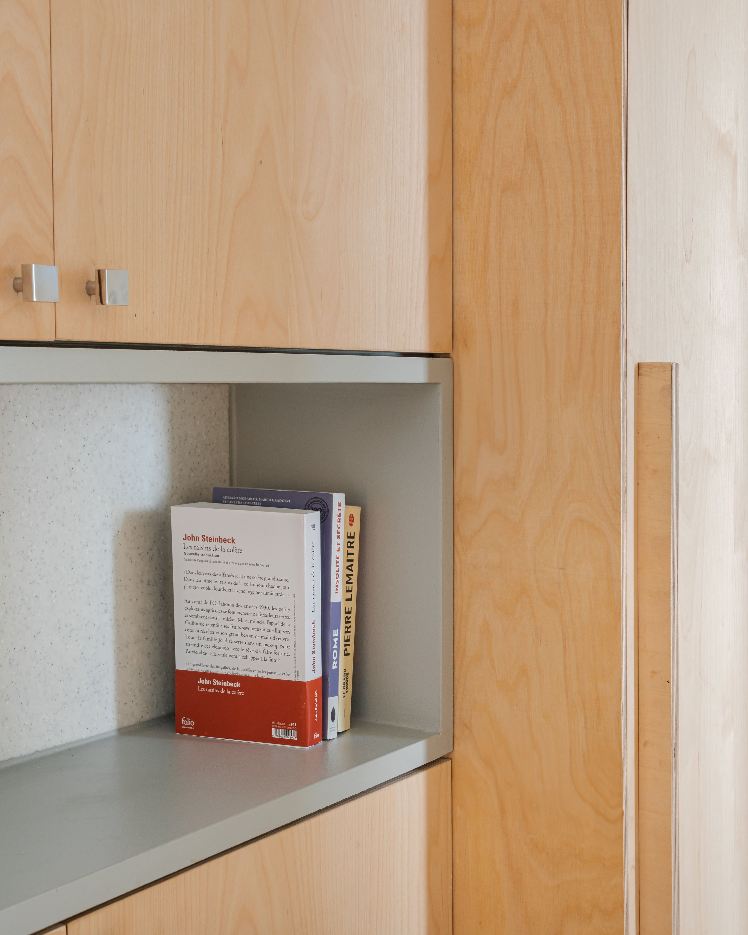 Une étagère contenant des livres dans une bibliothèque ou une salle de lecture, entourée de meubles en bois clair.