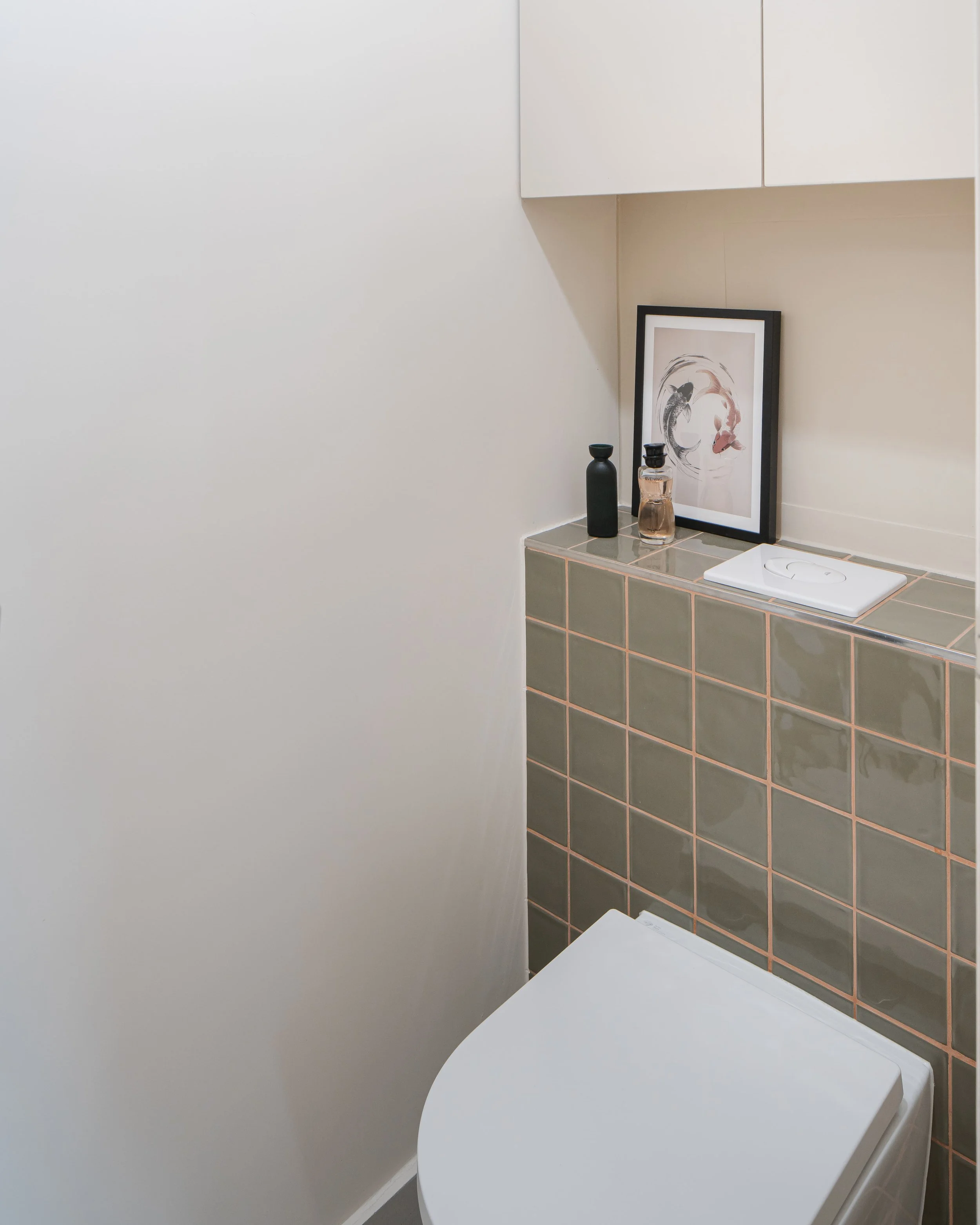 Coin toilette avec un lavabo, un téléphone, une affiche, et des bouteilles décoratives sur une étagère