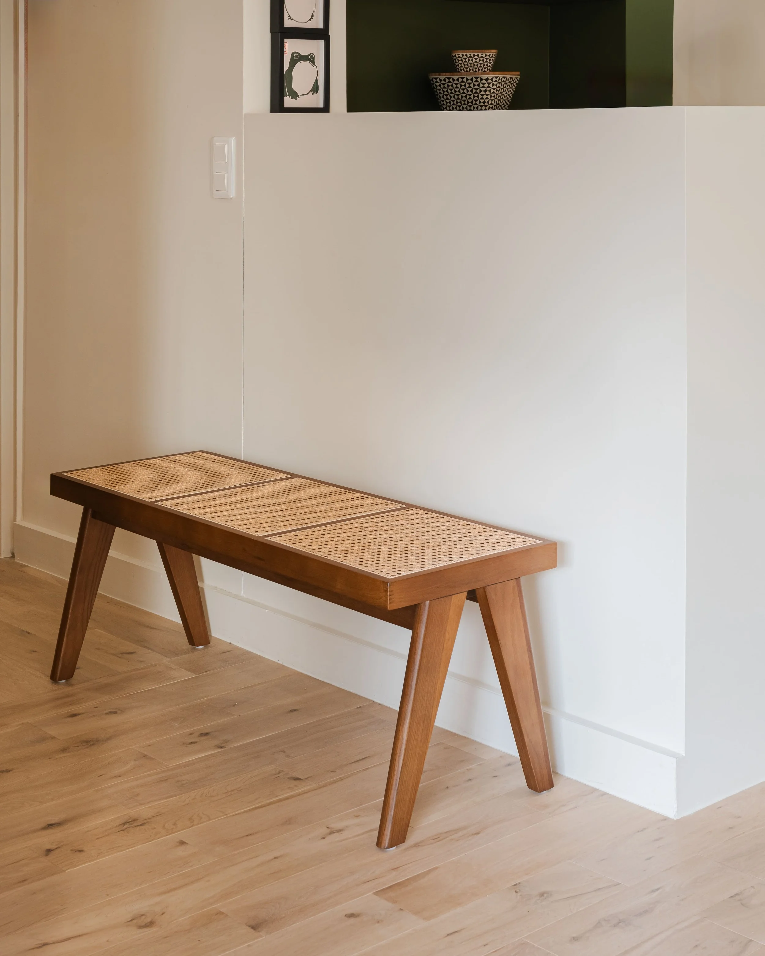 Banc en bois avec surface tissée en rotin dans une pièce aux murs blanc et sol en bois