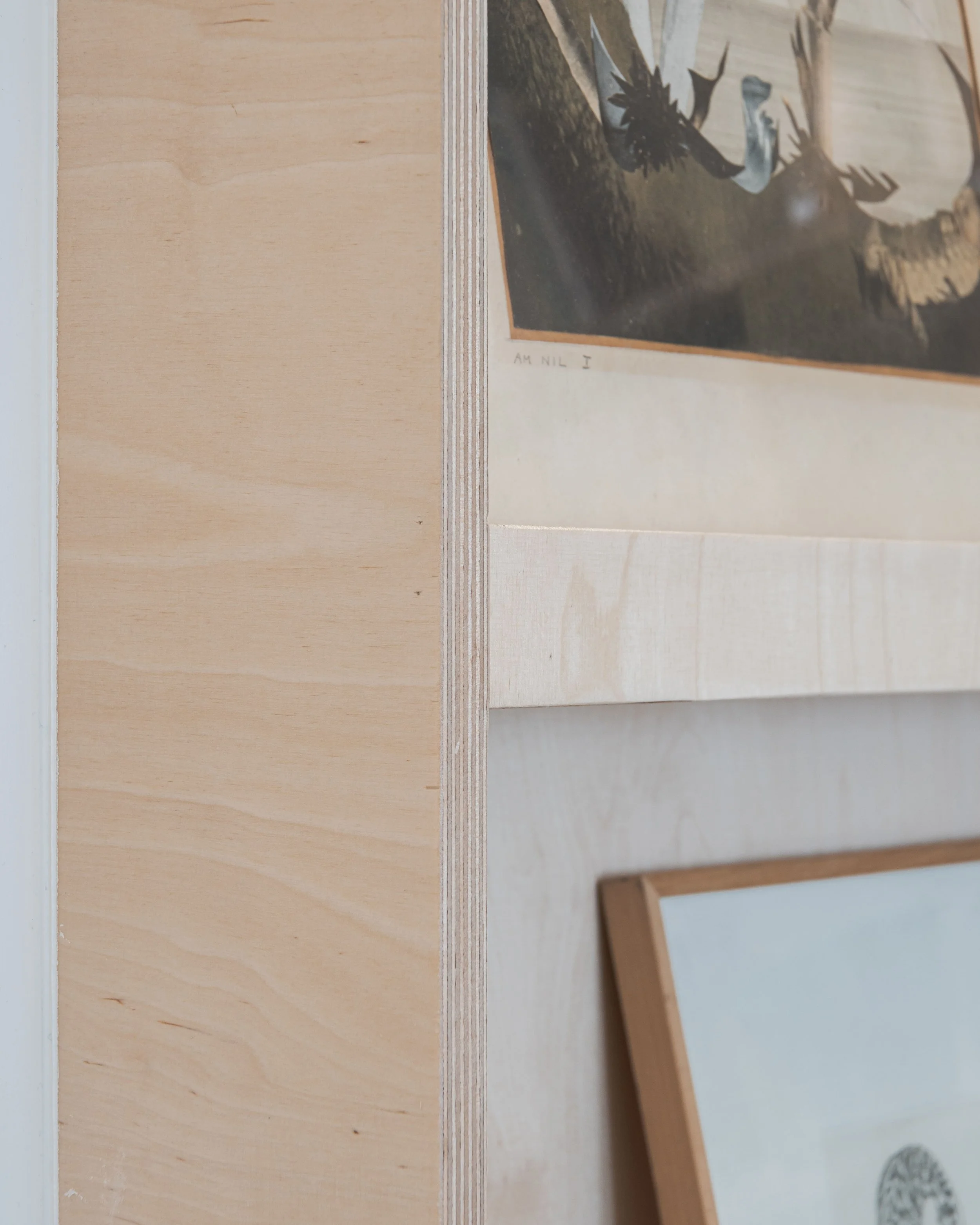 Une partie d'une pièce avec un mur en bois clair et deux cadres accrochés, l'un contenant une image sombre et l'autre un dessin ou une photographie encadrée en bois clair.