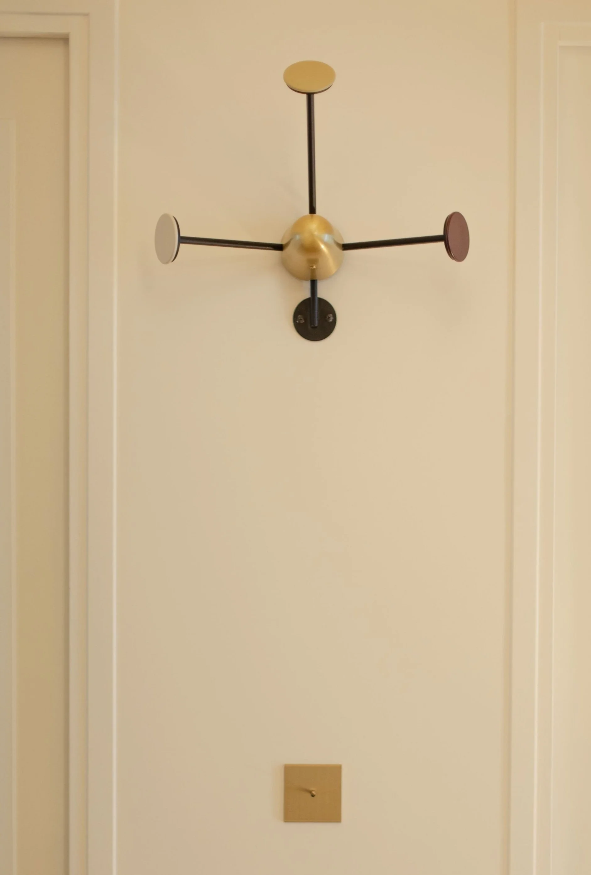 Horloge murale moderne avec trois bras et un centre en forme de boule, fixée sur un mur beige.