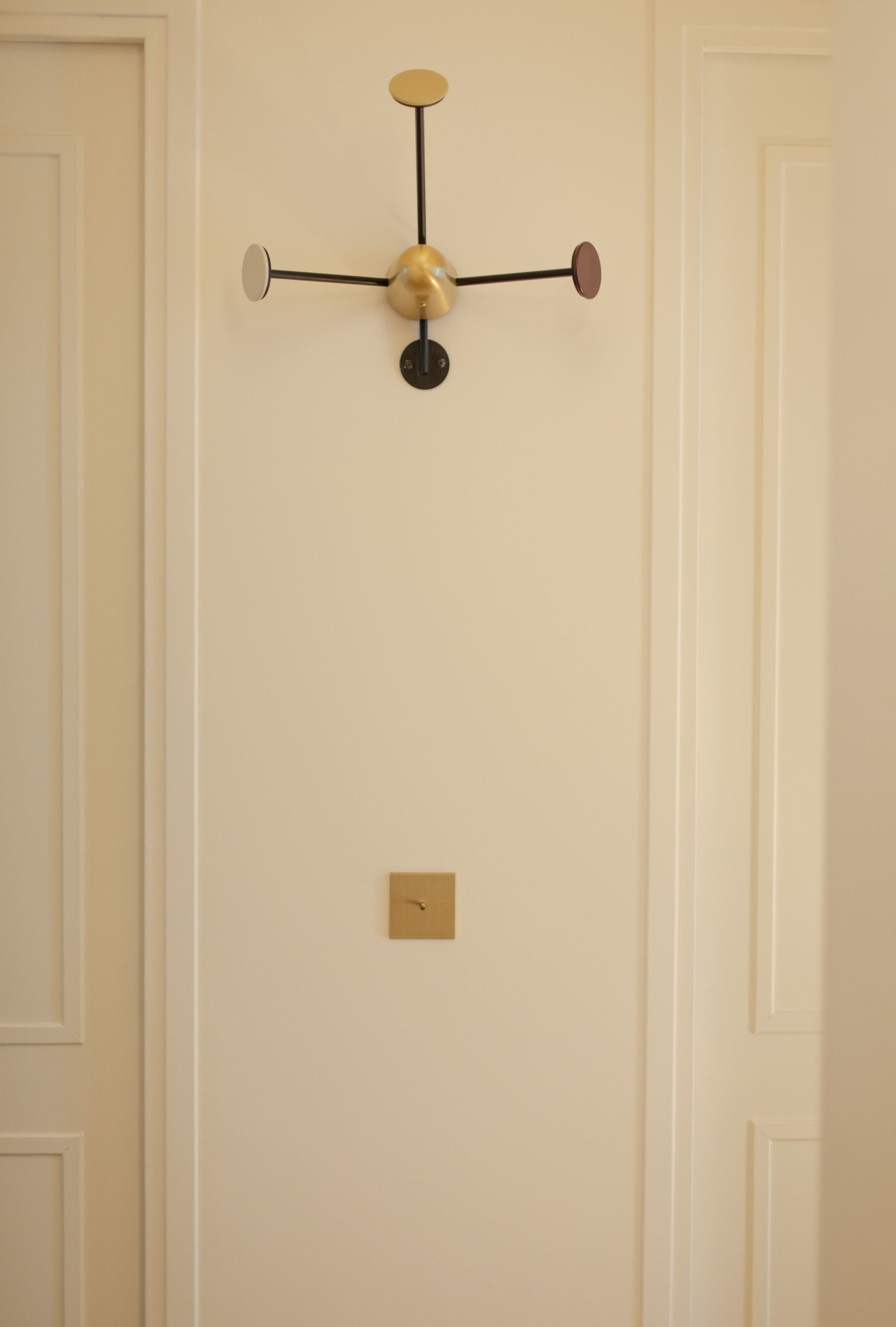 Un mur blanc avec un appareil d'éclairage moderne à quatre bras et une prise électrique en dessous.