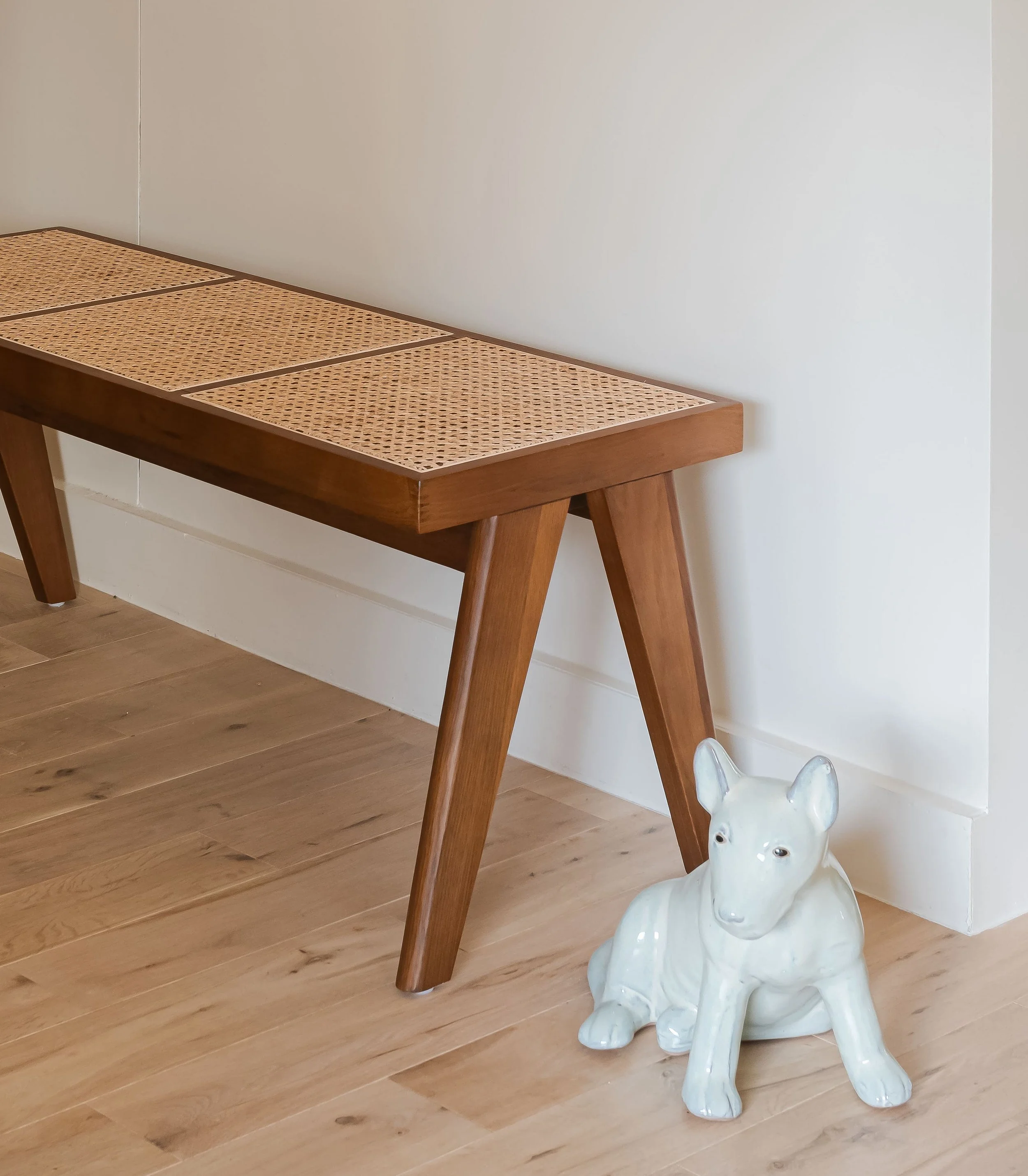 Une table en bois avec un dessus en rotin, et une sculpture en céramique d'un chien Basenji blanc assis.