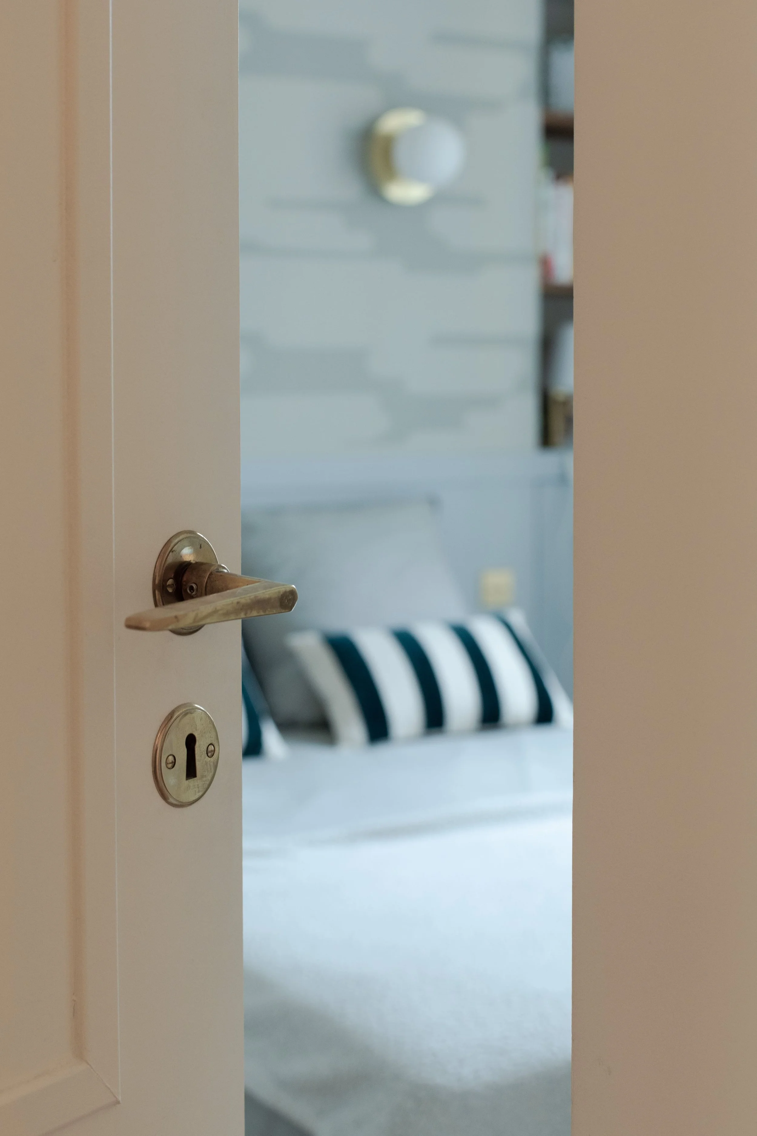 Une porte entrouverte révélant une chambre avec un lit, des coussins à rayures noires et blanches, et une décoration murale en forme de lune. 