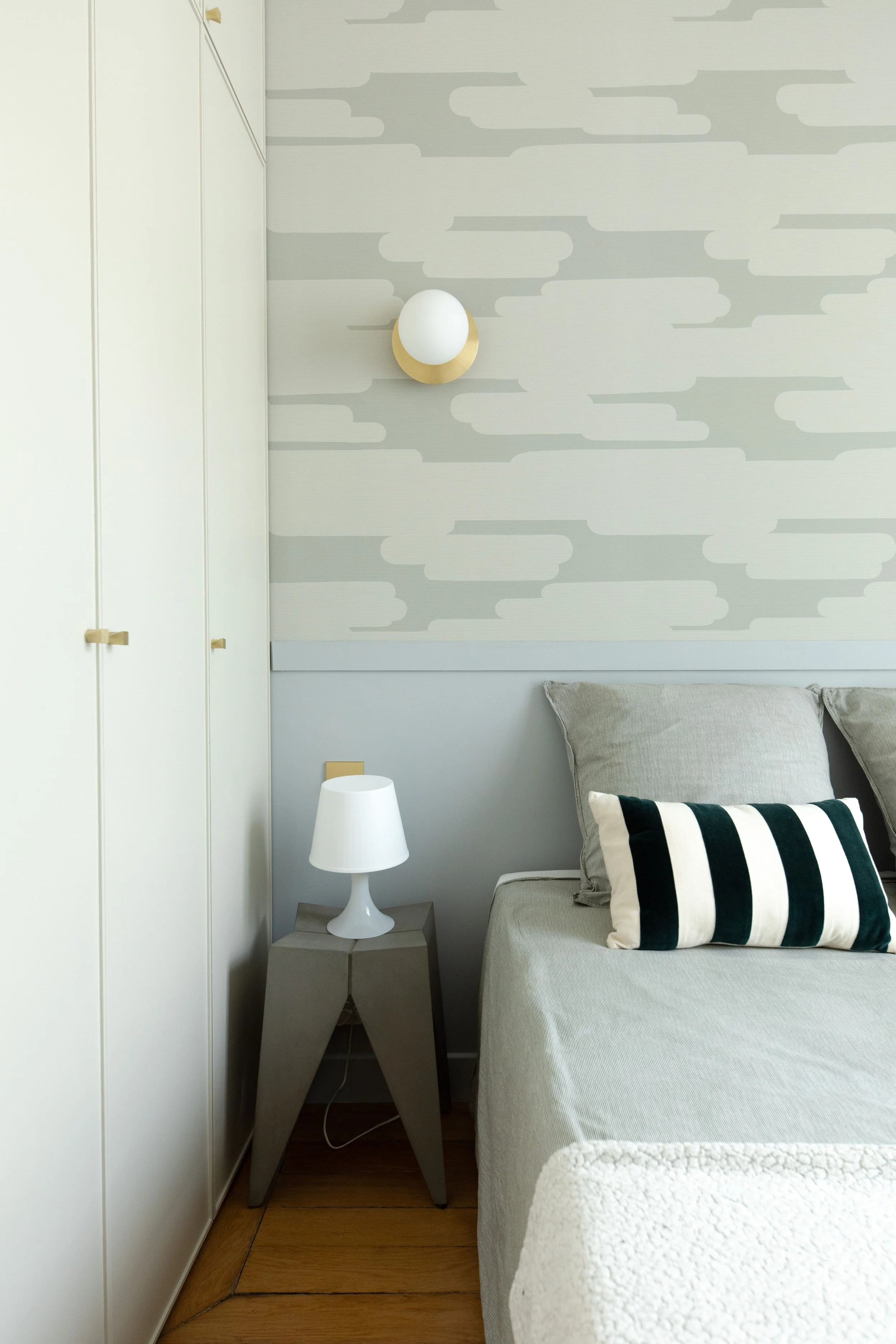 Coin de chambre avec un lit, une table de chevet avec lampe, un mur avec un design graphique et un luminaire mural