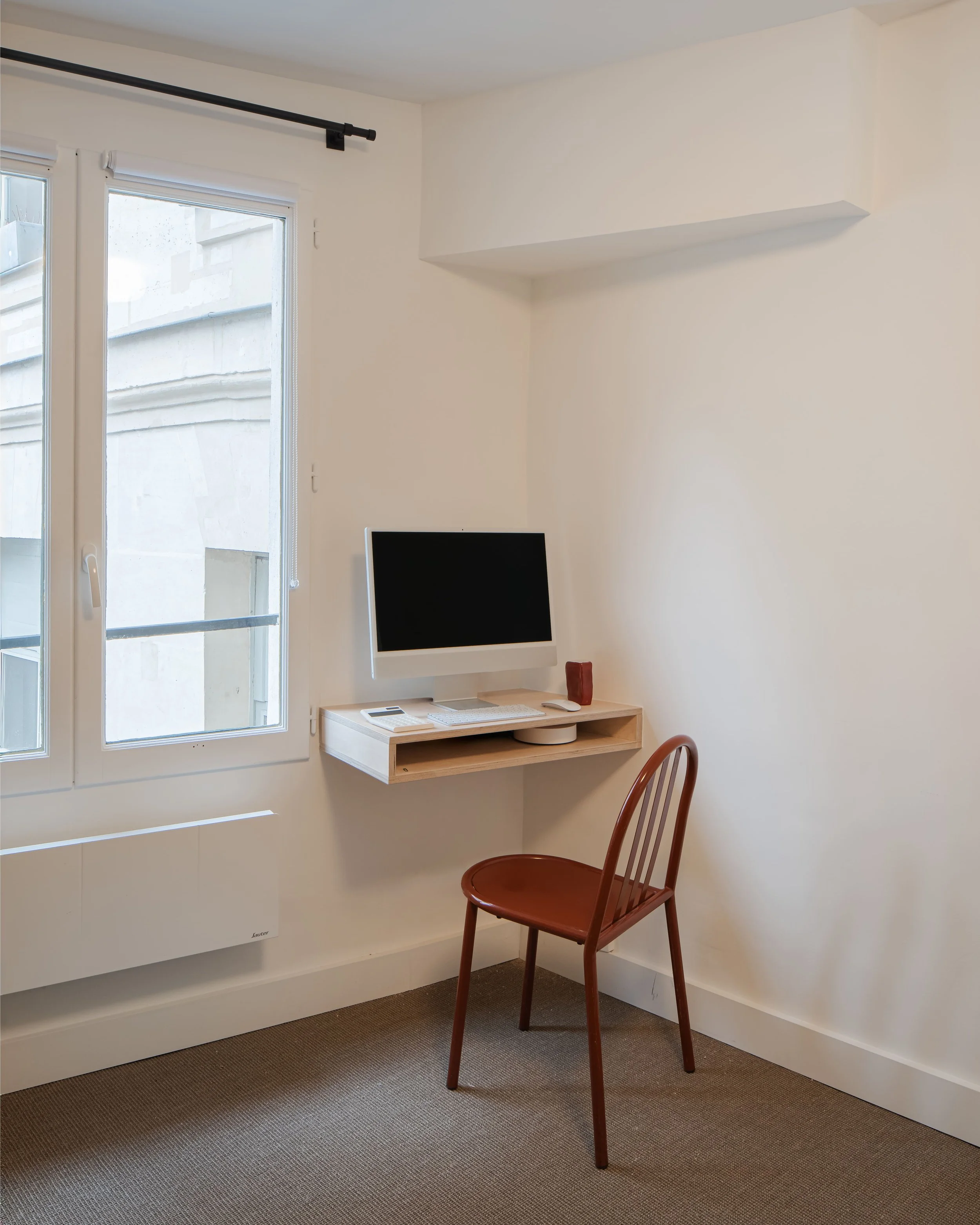 Coin bureau avec un ordinateur, une chaise en bois, une fenêtre et un mur blanc.