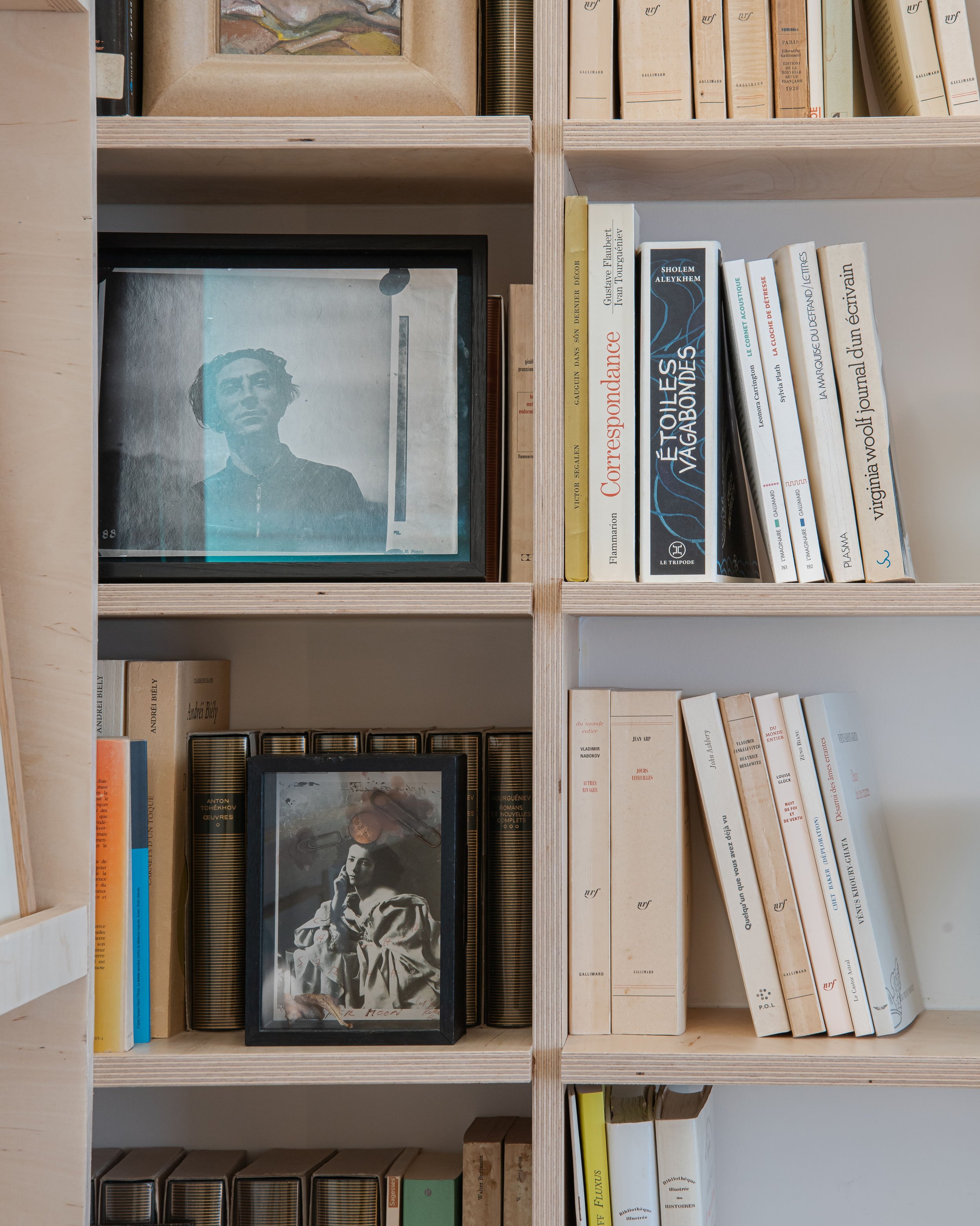 Une étagère en bois contenant des livres et deux cadres photo, l'un avec une image en noir et blanc d'une femme et l'autre avec un portrait en couleur.