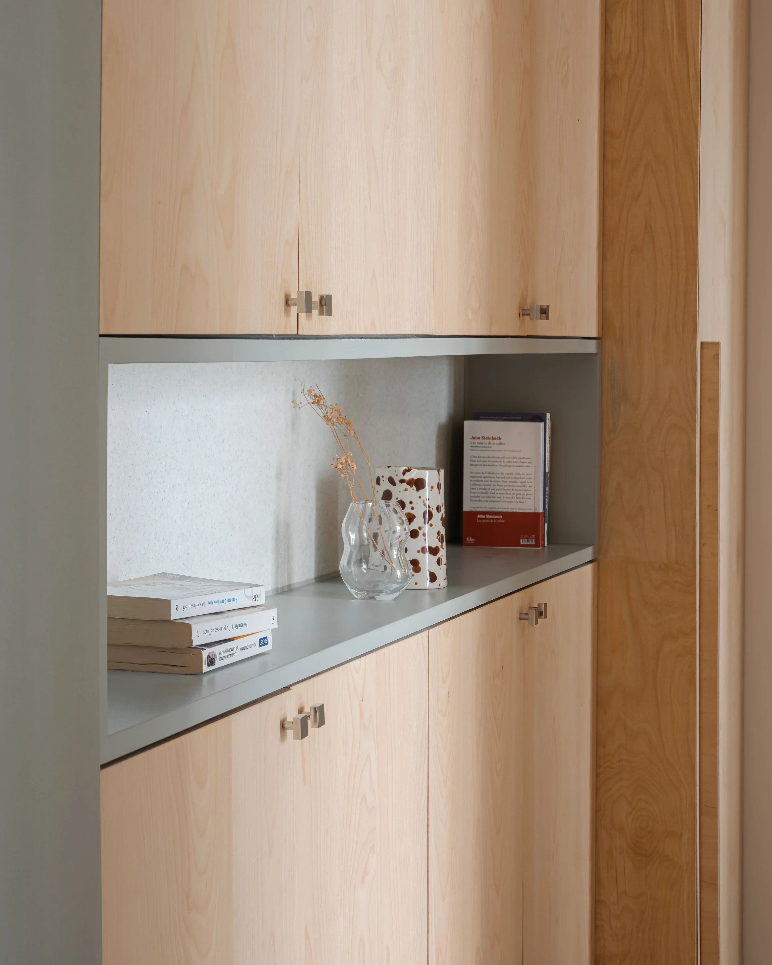 Étagère en bois clair avec des livres, un vase en verre avec des branches sèches, et un vase décoratif avec des taches