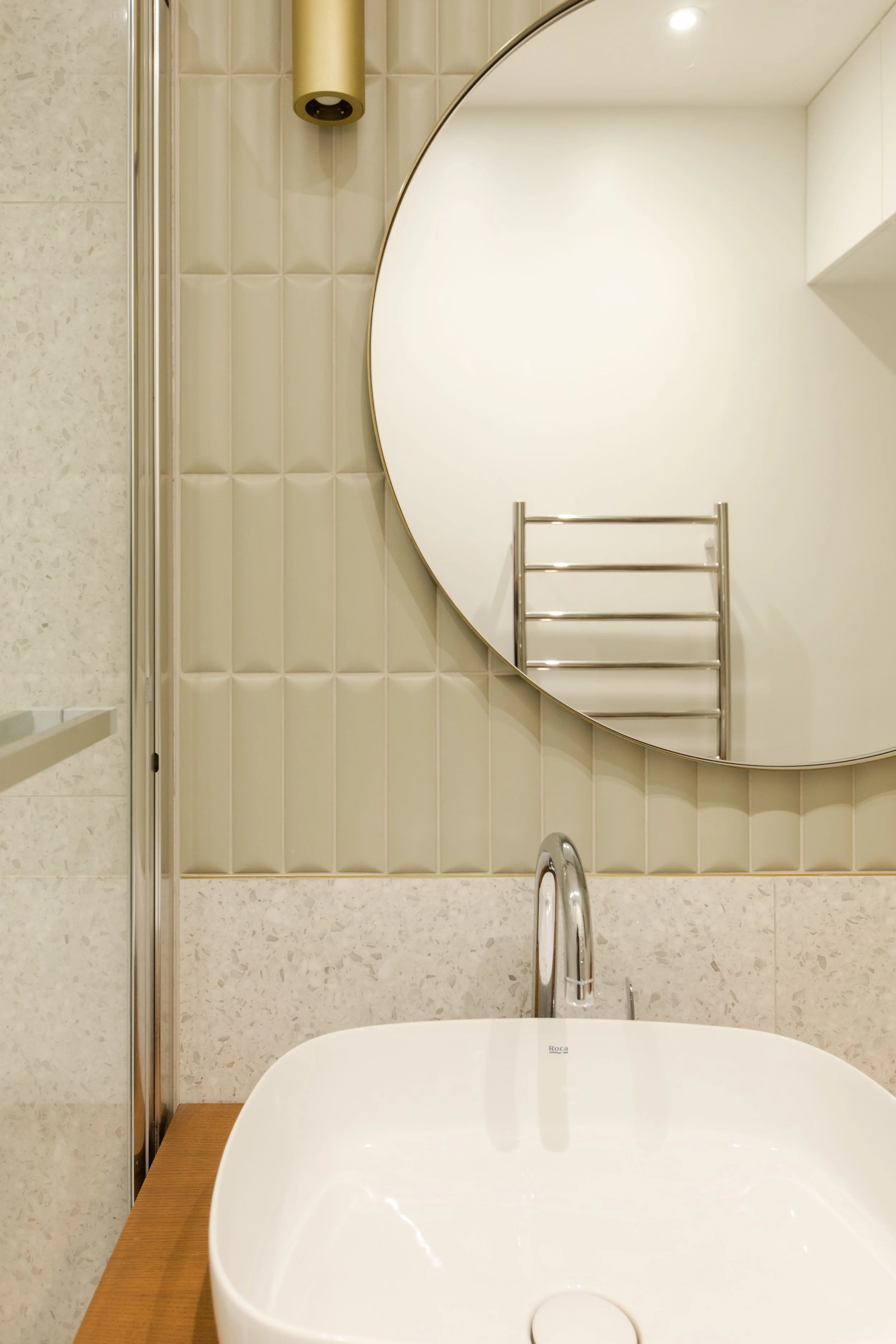 Miroir rond au-dessus d'un lavabo blanc avec un miroir et un radiateur en acier inoxydable visible dans la salle de bain.