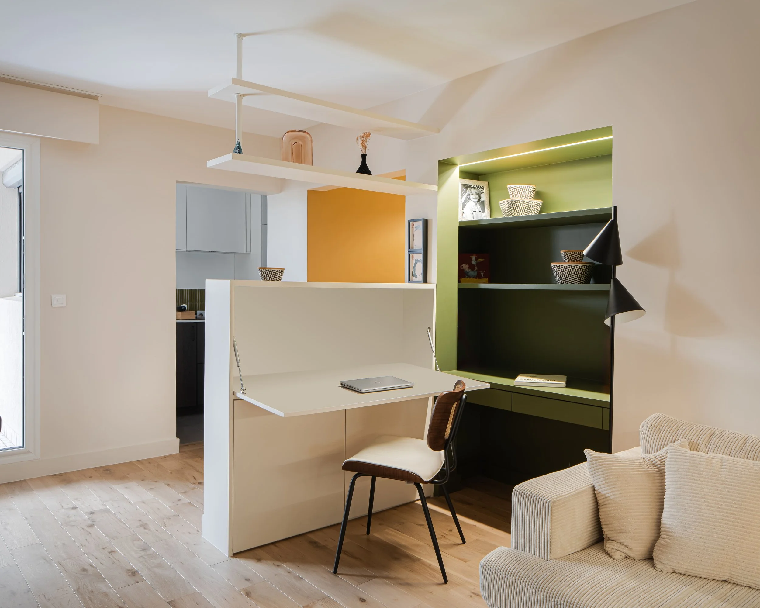 Salon avec bureau blanc, étagère noire, canapé beige, et décoration colorée, dans un style moderne.