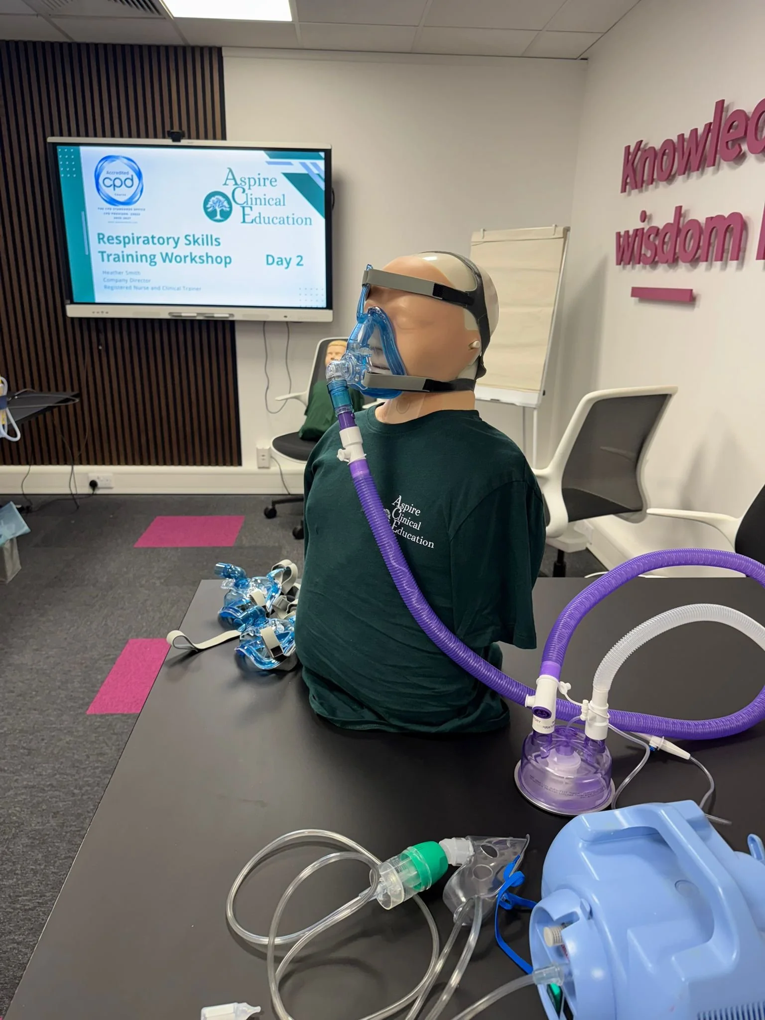 Screen displaying Respiratory Workshop Day 2 and sim manikin with non invasive ventilation mask on, nebuliser machine and other kit