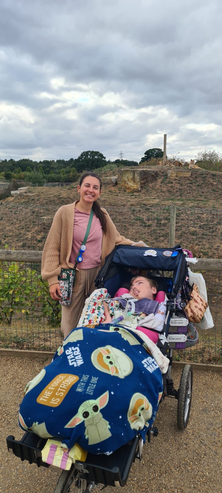 Heather and her nursing client at the zoo with lions on the hill behind