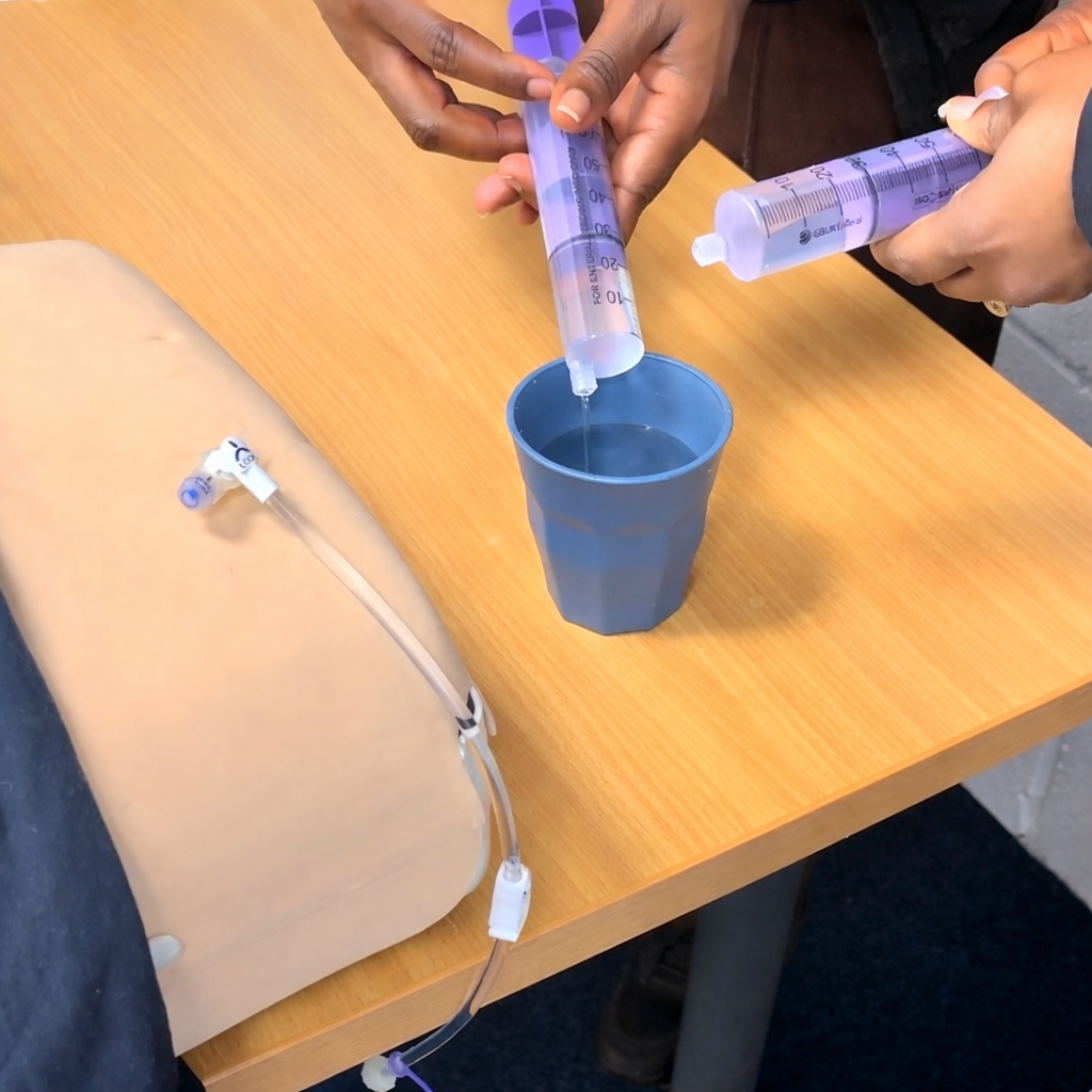 two staff practicing flushing with 60ml enteral syringes