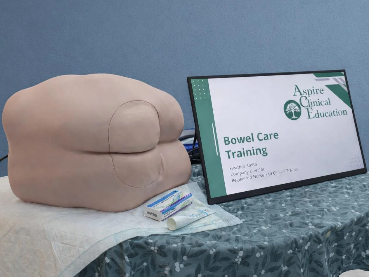 Bowel care simulator on a table with a monitor showing training presentation