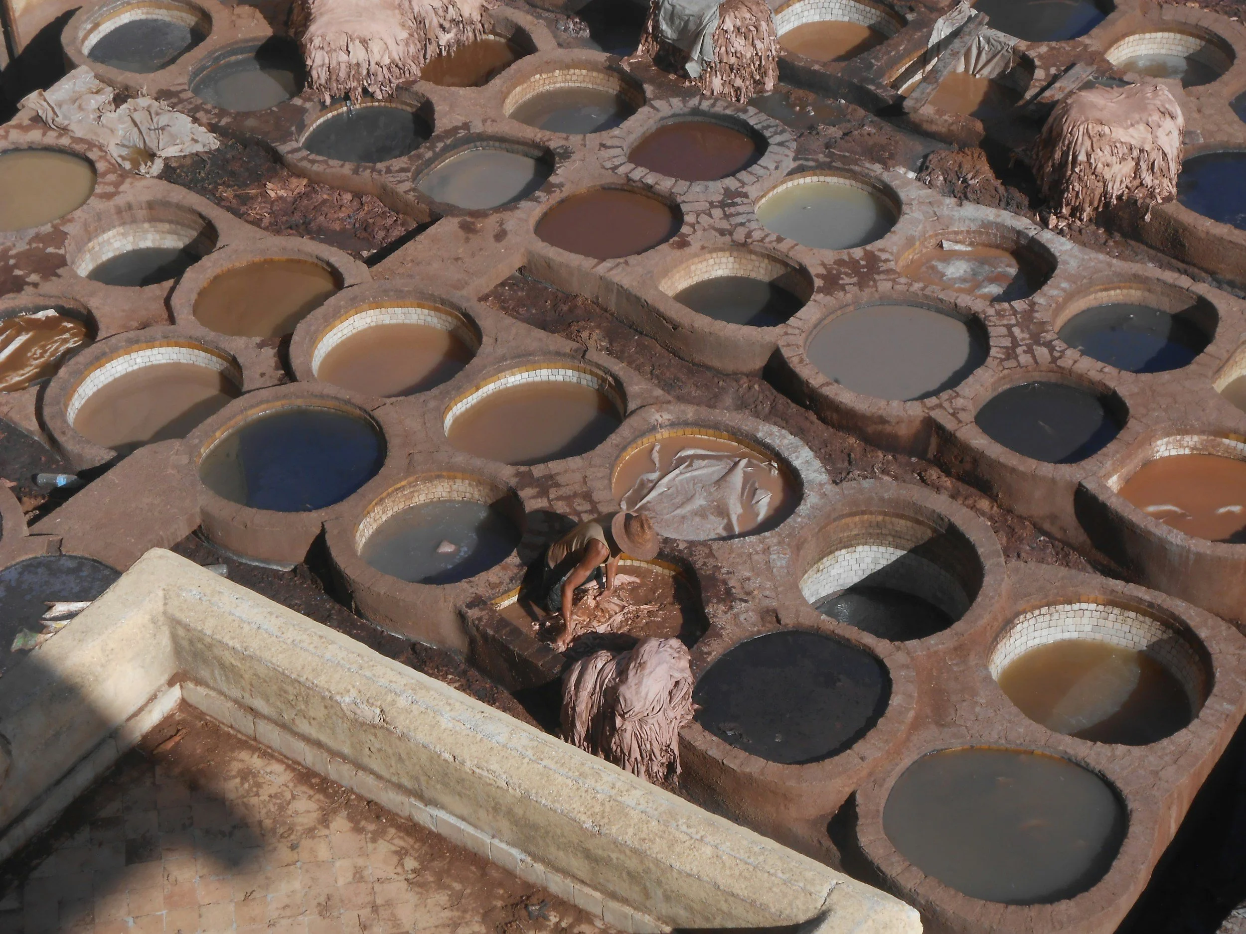 A traditional tannery with numerous circular vats filled with various colored liquids used for processing animal hides, with workers tending to the vats.