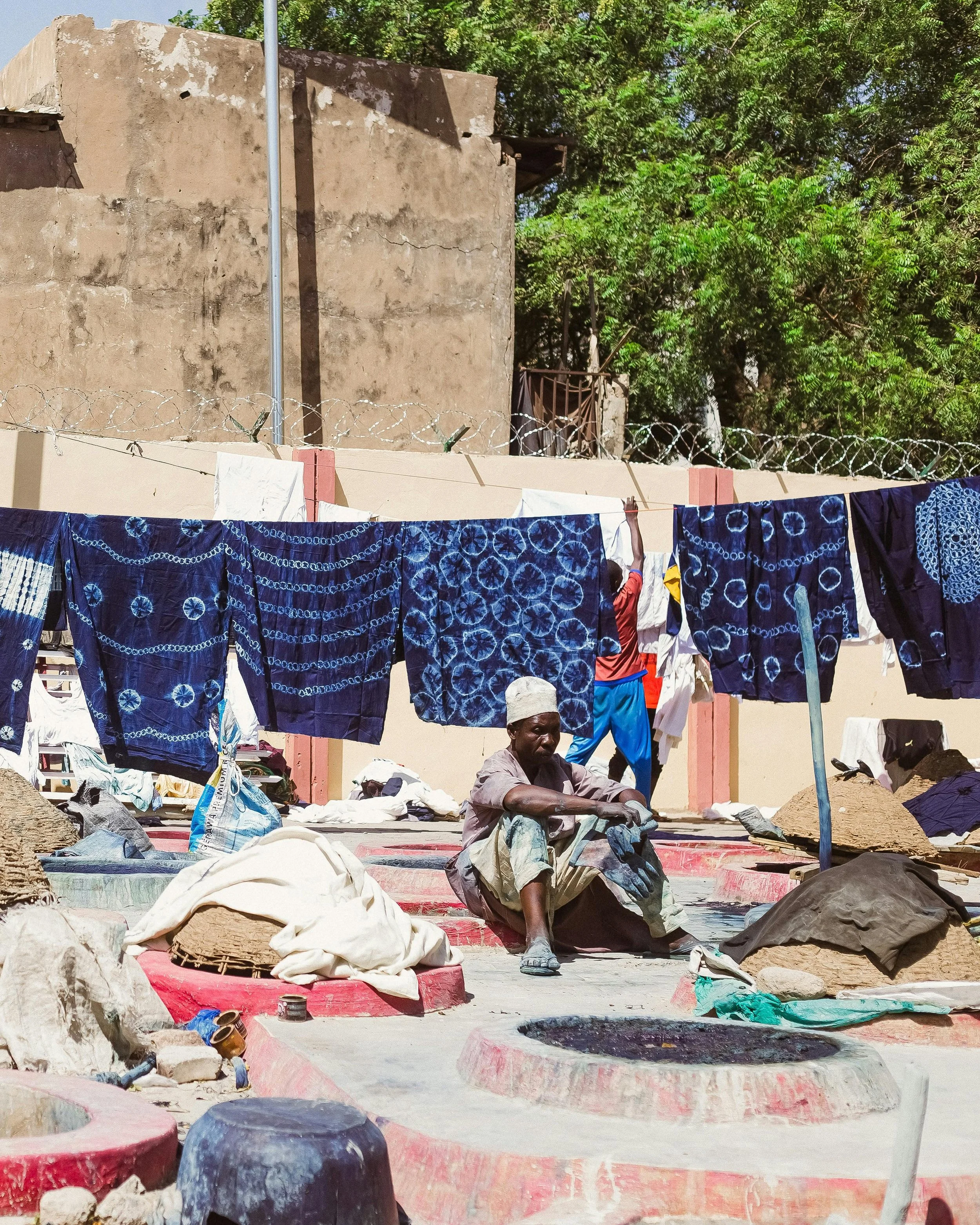 A man sits under drying indigo dyed fabrics