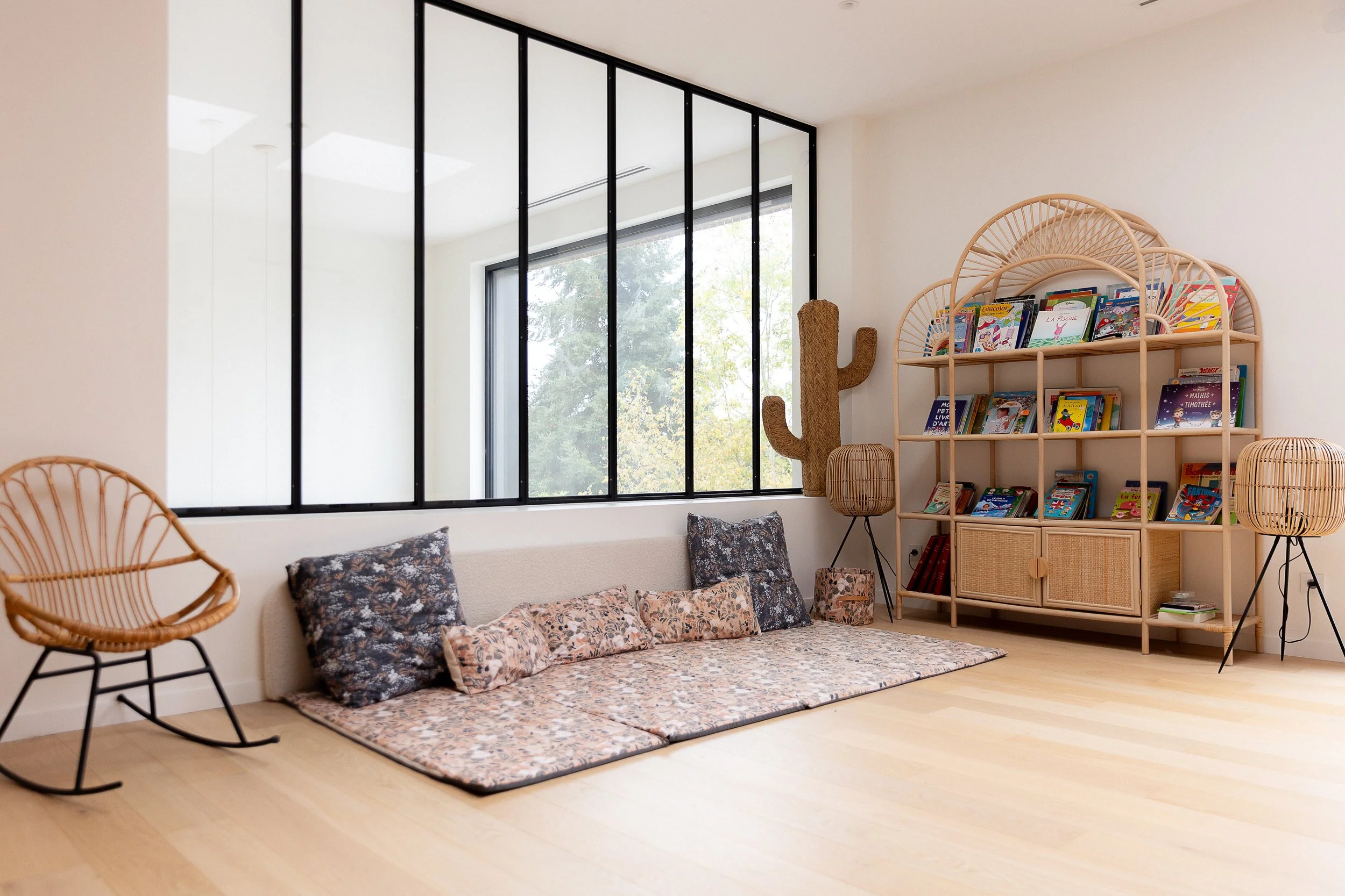 Salle de lecture ouverte sur le salon, avec tapis au sol et mobilier en rotin