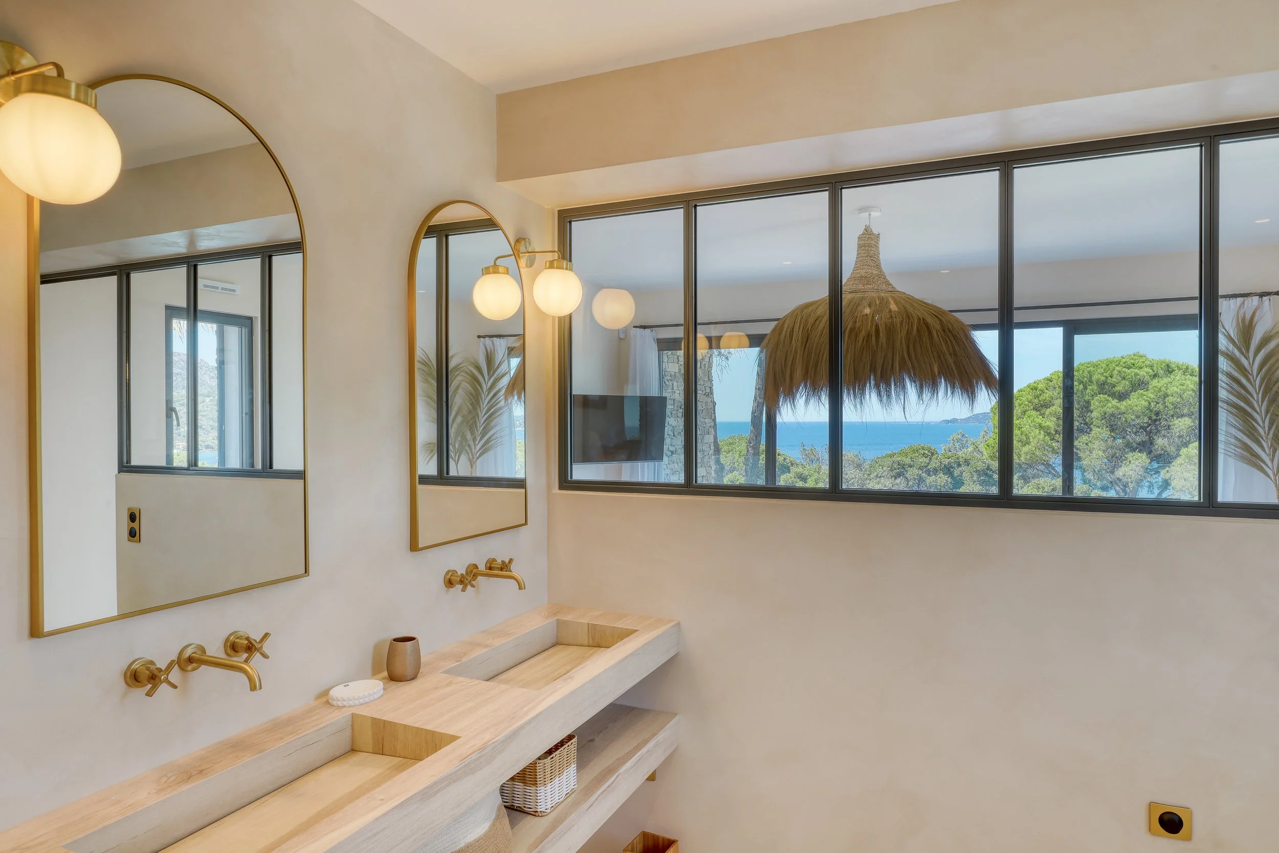 Salle de bain en béton ciré, meuble vasque en bois, avec verrière donnant sur la chambre et sa vue mer.