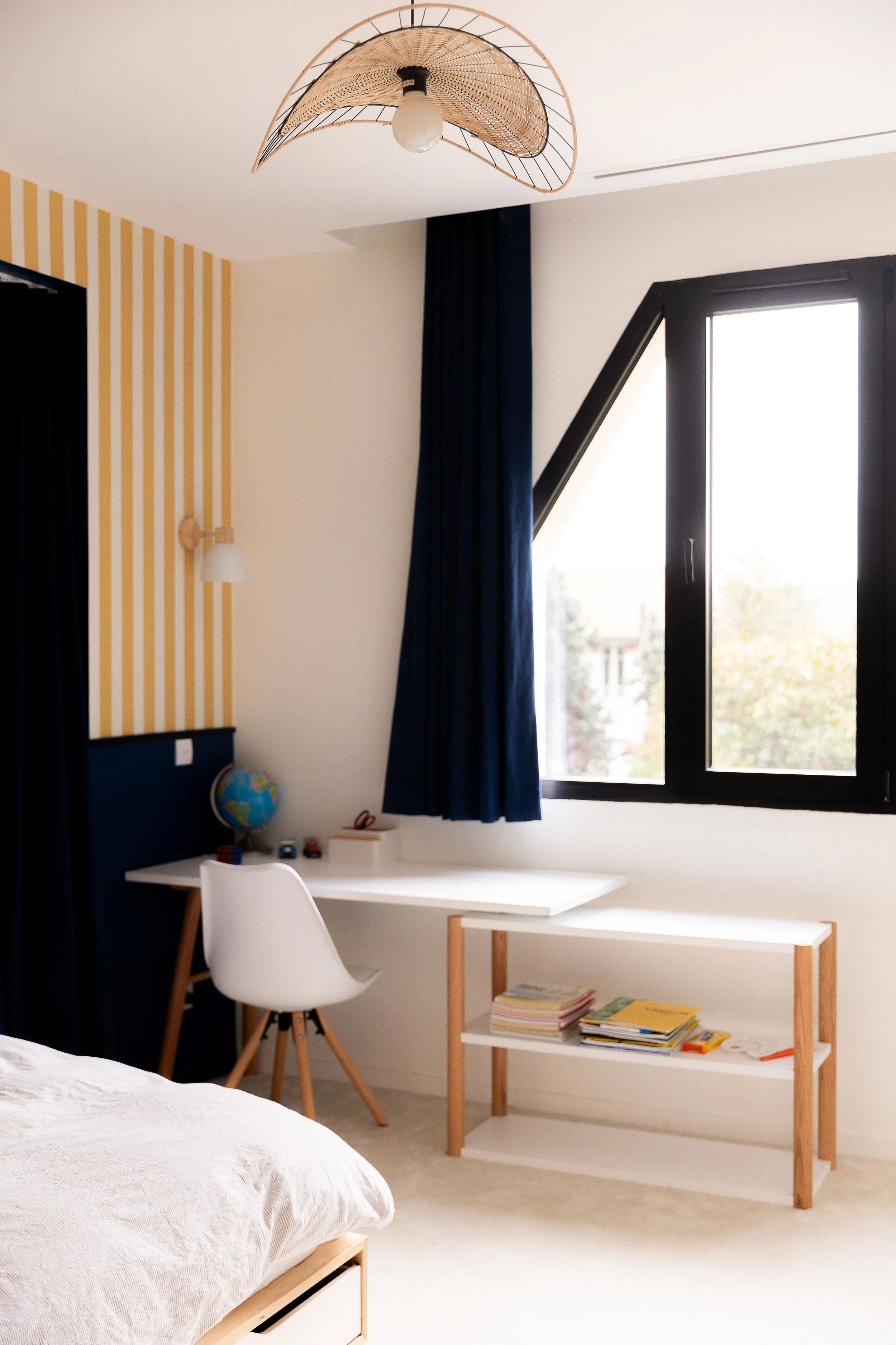 Chambre rénovée avec sous bassement en peinture bleu et papier peint rayé jaune et blanc. Rideaux assortis.