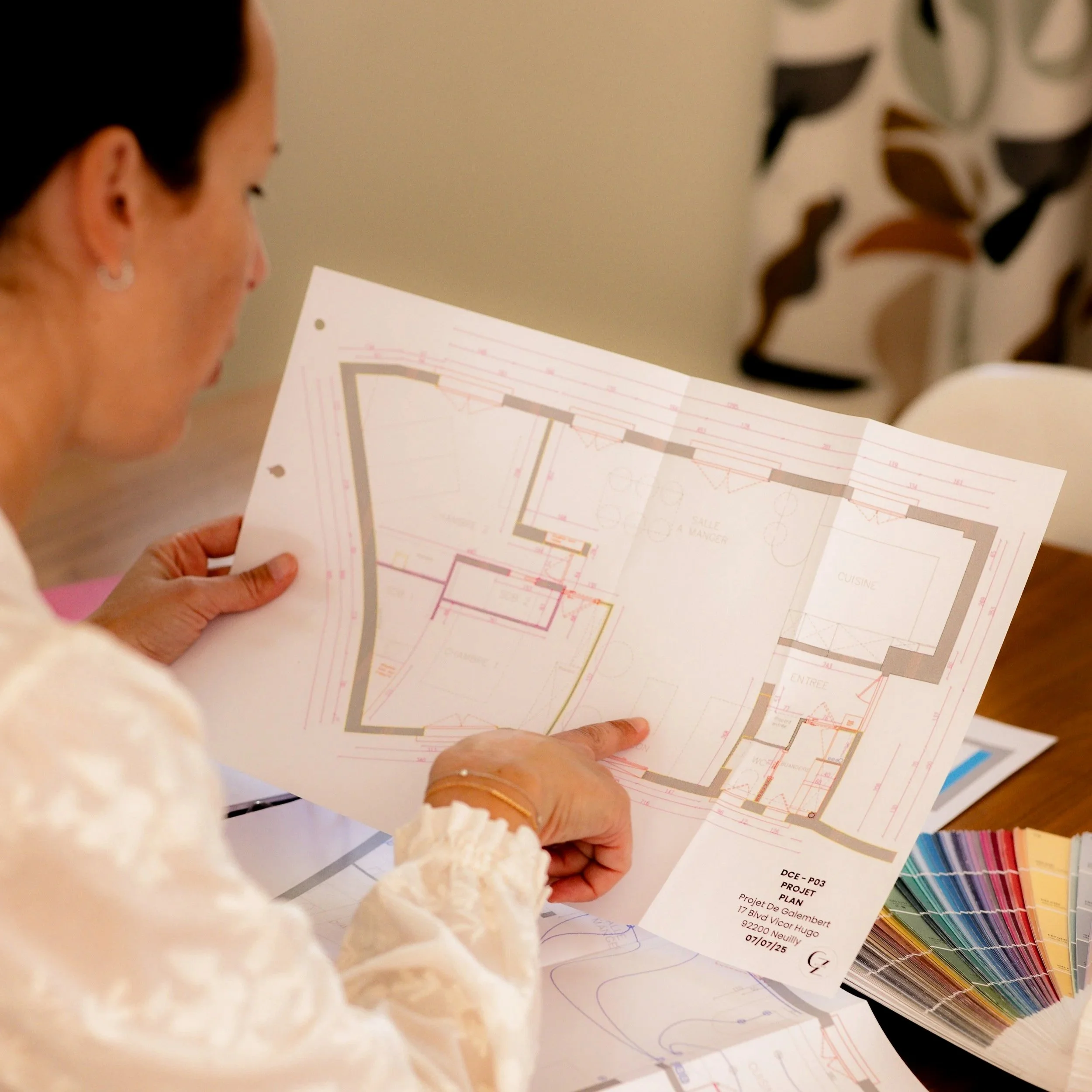 Une femme regarde des plans et des échantillons de couleurs, probablement pour un projet de construction ou de décoration intérieure.