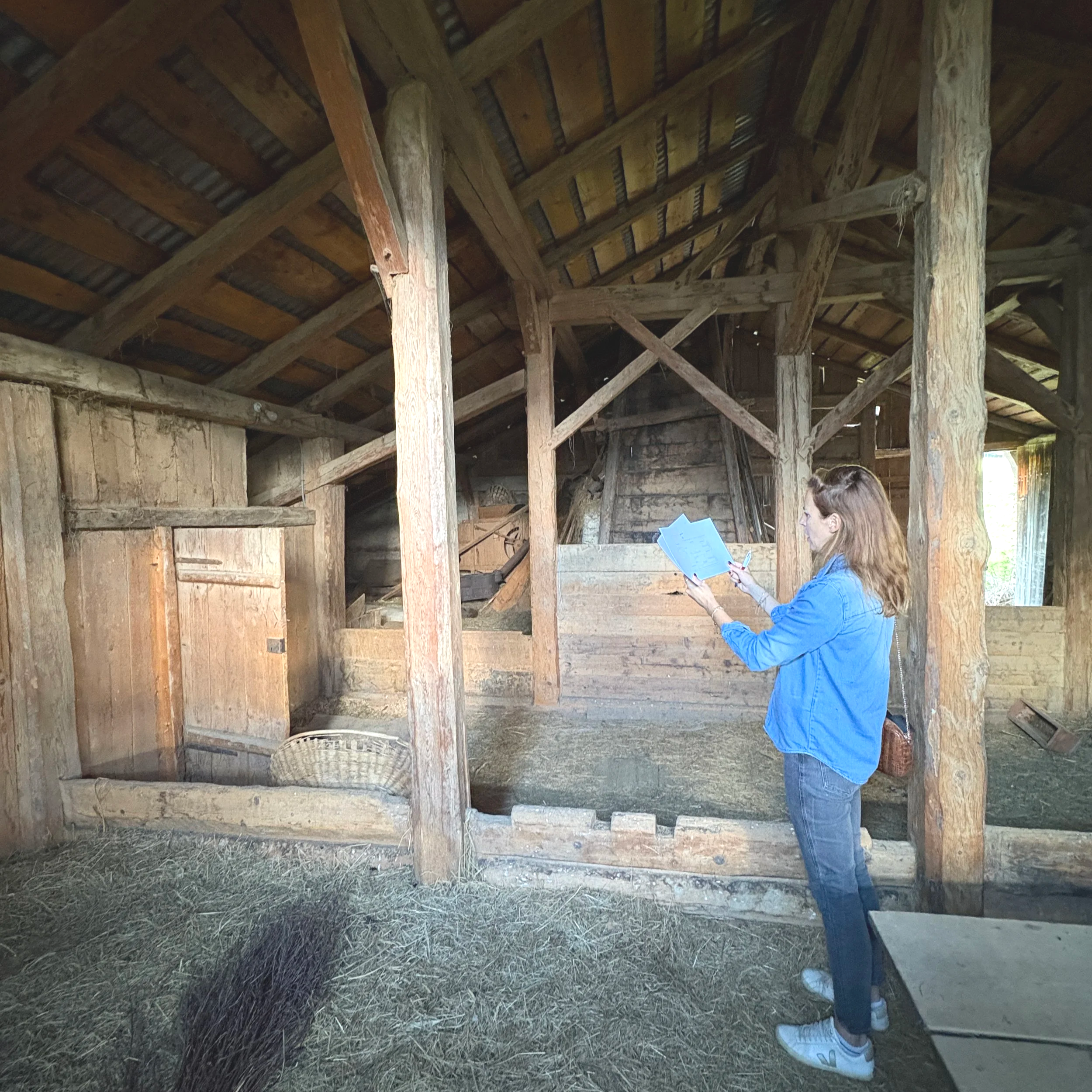Une femme en jean et veste bleue regarde un document dans un bâtiment en bois rustique.