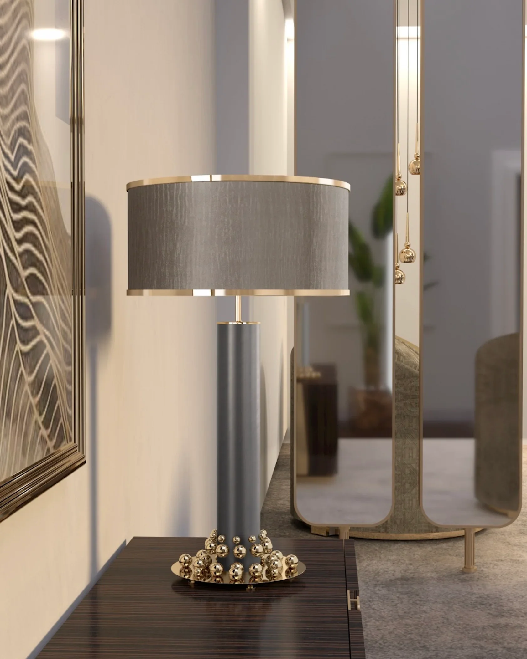 A modern table lamp with a gray cylindrical shade and metallic base decorated with gold-colored balls, placed on a wooden table next to a mirror.