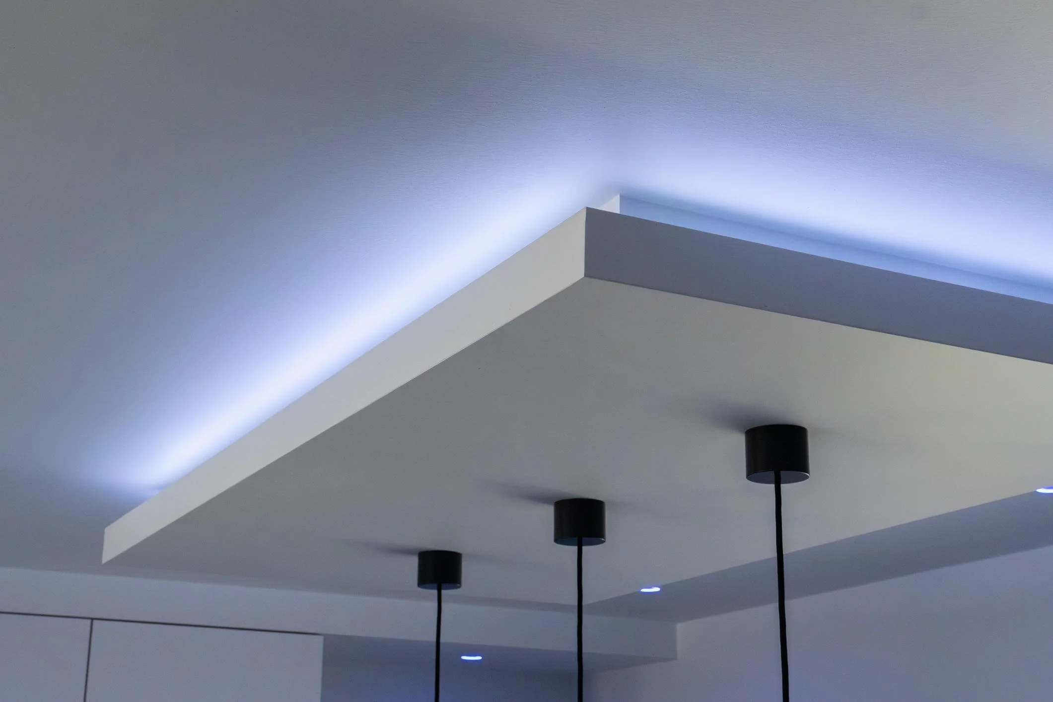 Modern ceiling with integrated lighting and three black pendant lights hanging down.
