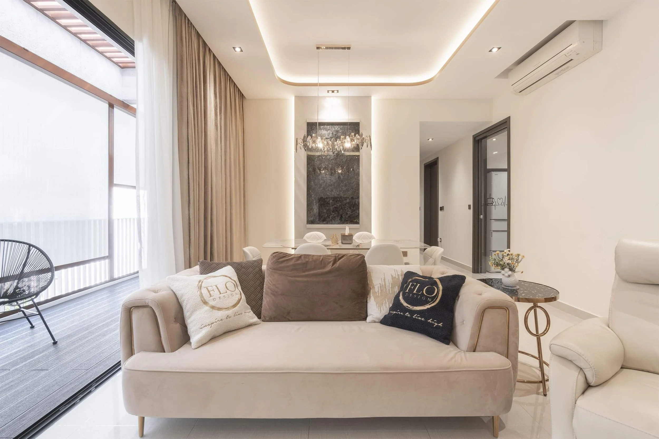 Modern living room with beige sofa, decorative pillows, and a balcony with glass sliding doors, white walls, and contemporary decor.