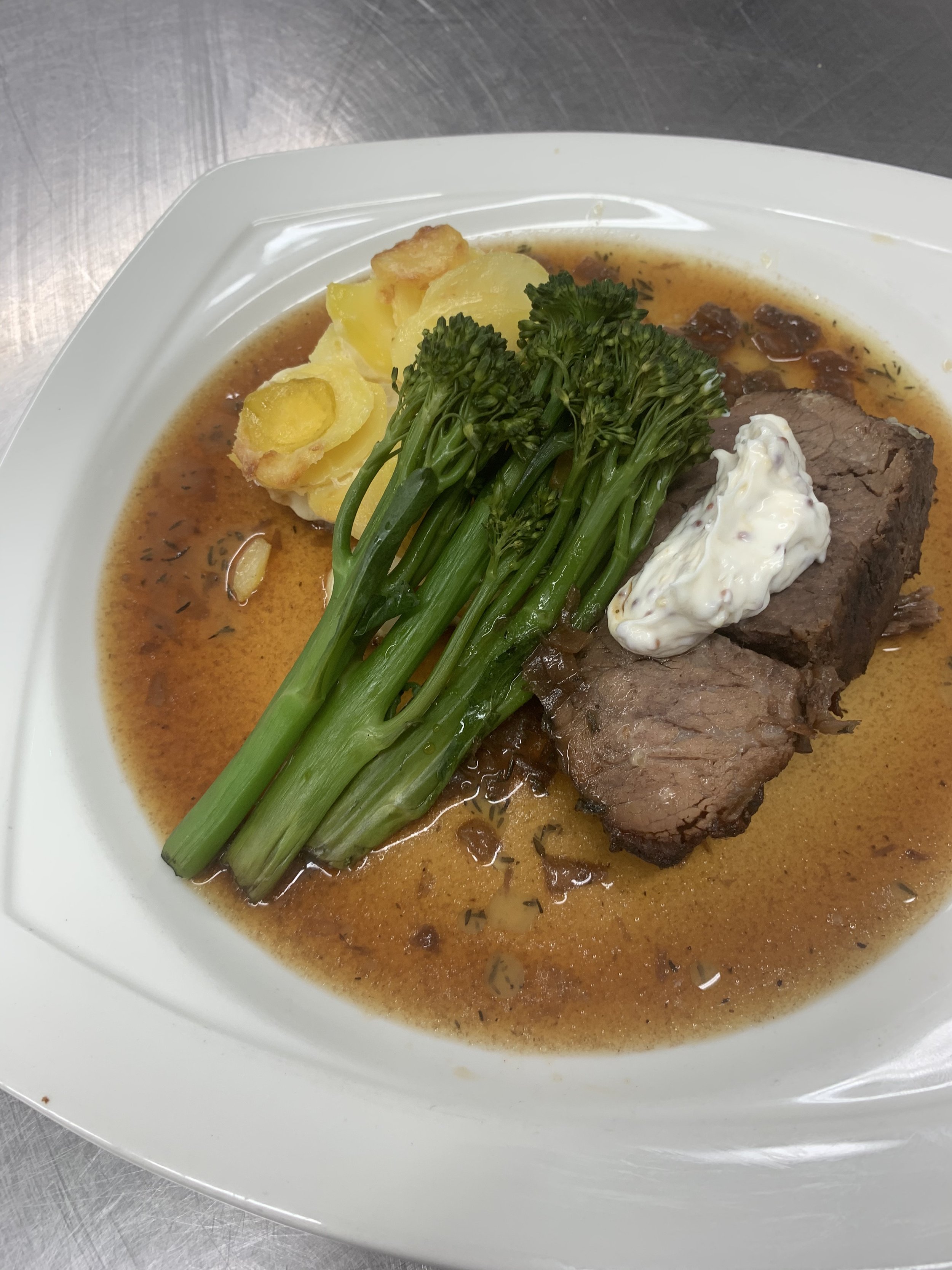 Plate of beef stew with green broccolini, mashed potatoes, and gravy.