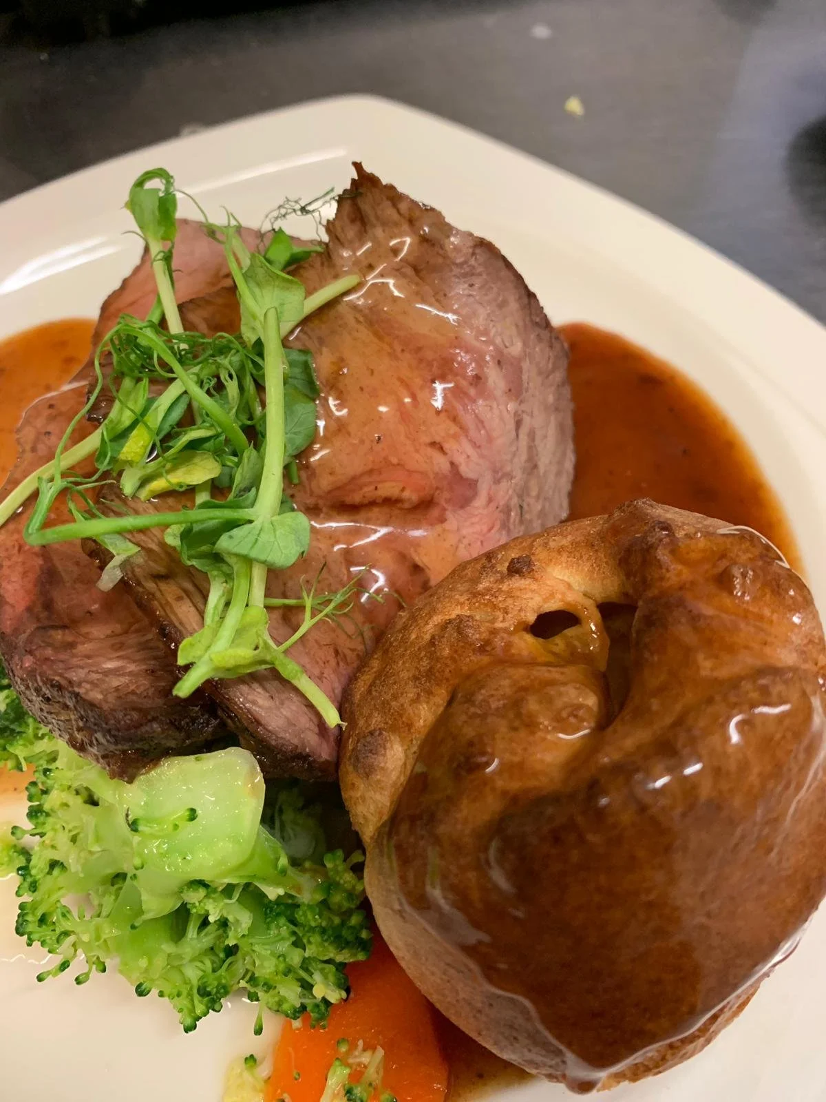 A plate with roasted beef, a gravy, a baked potato, and steamed broccoli.