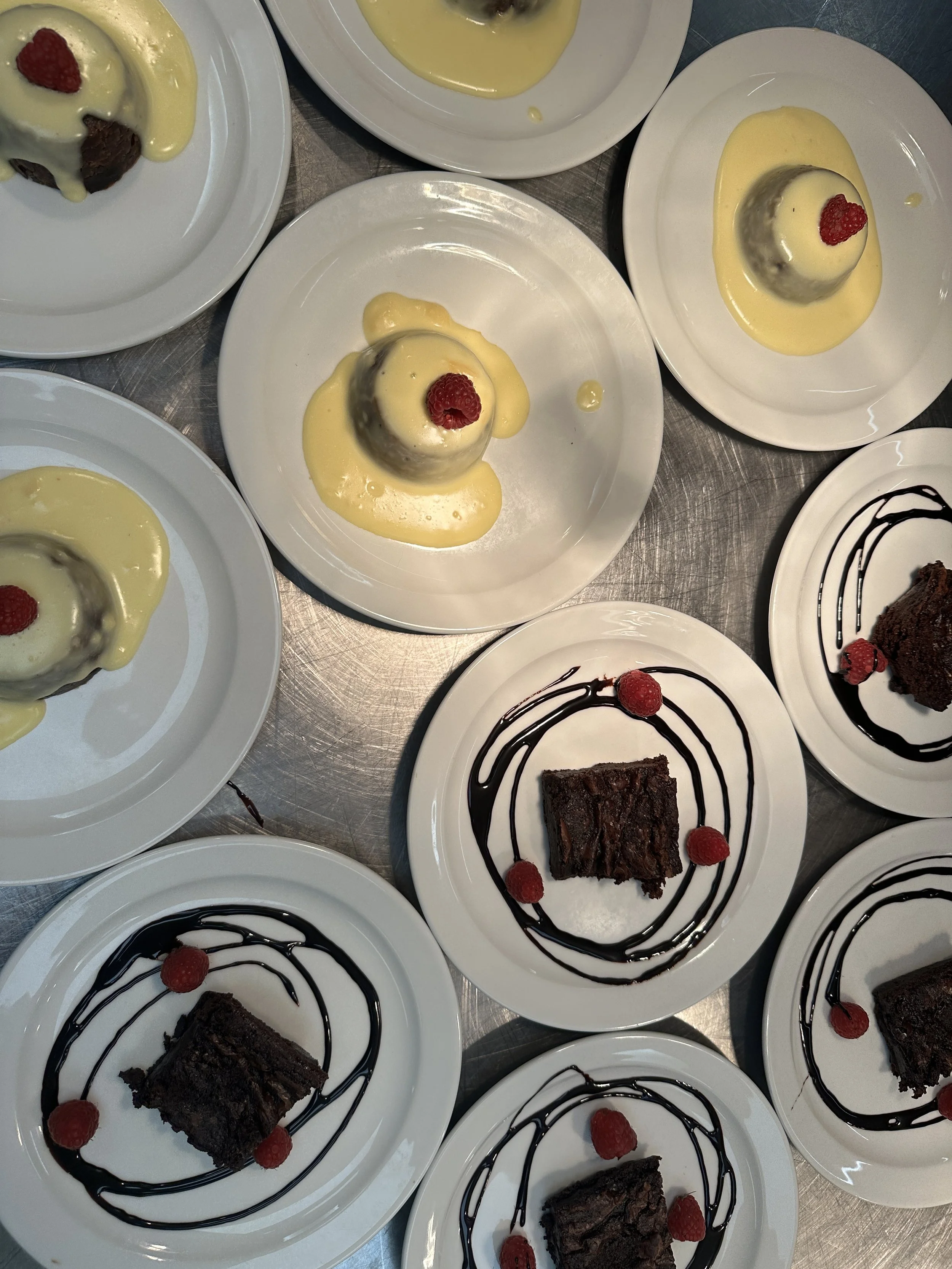 Dessert plates with chocolate cake and raspberries, and plates with ice cream topped with raspberries and yellow sauce.