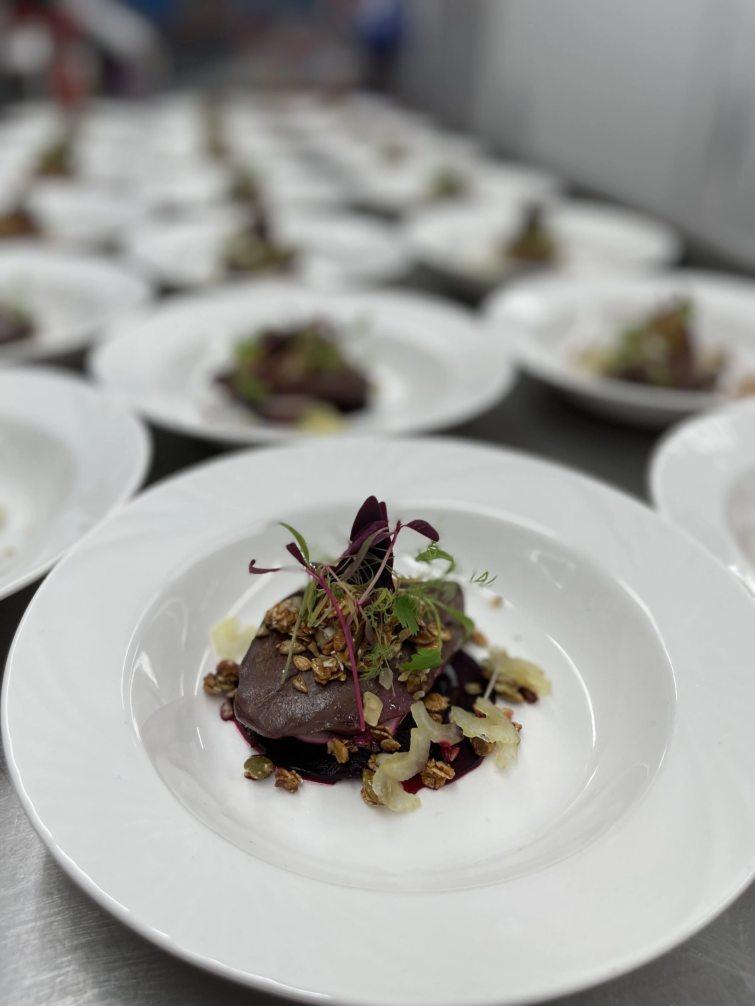 Plated dish with cooked meat, garnished with microgreens, nuts, and shredded vegetables on a white plate.