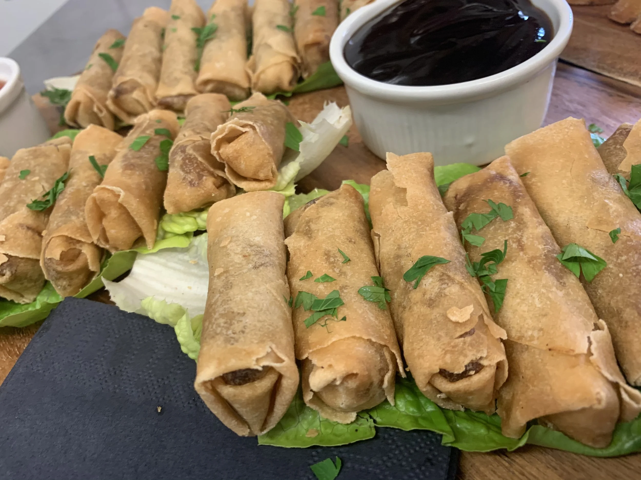 A plate of fried spring rolls garnished with chopped green herbs, with a side of dipping sauce and a small bowl of dark soy sauce.