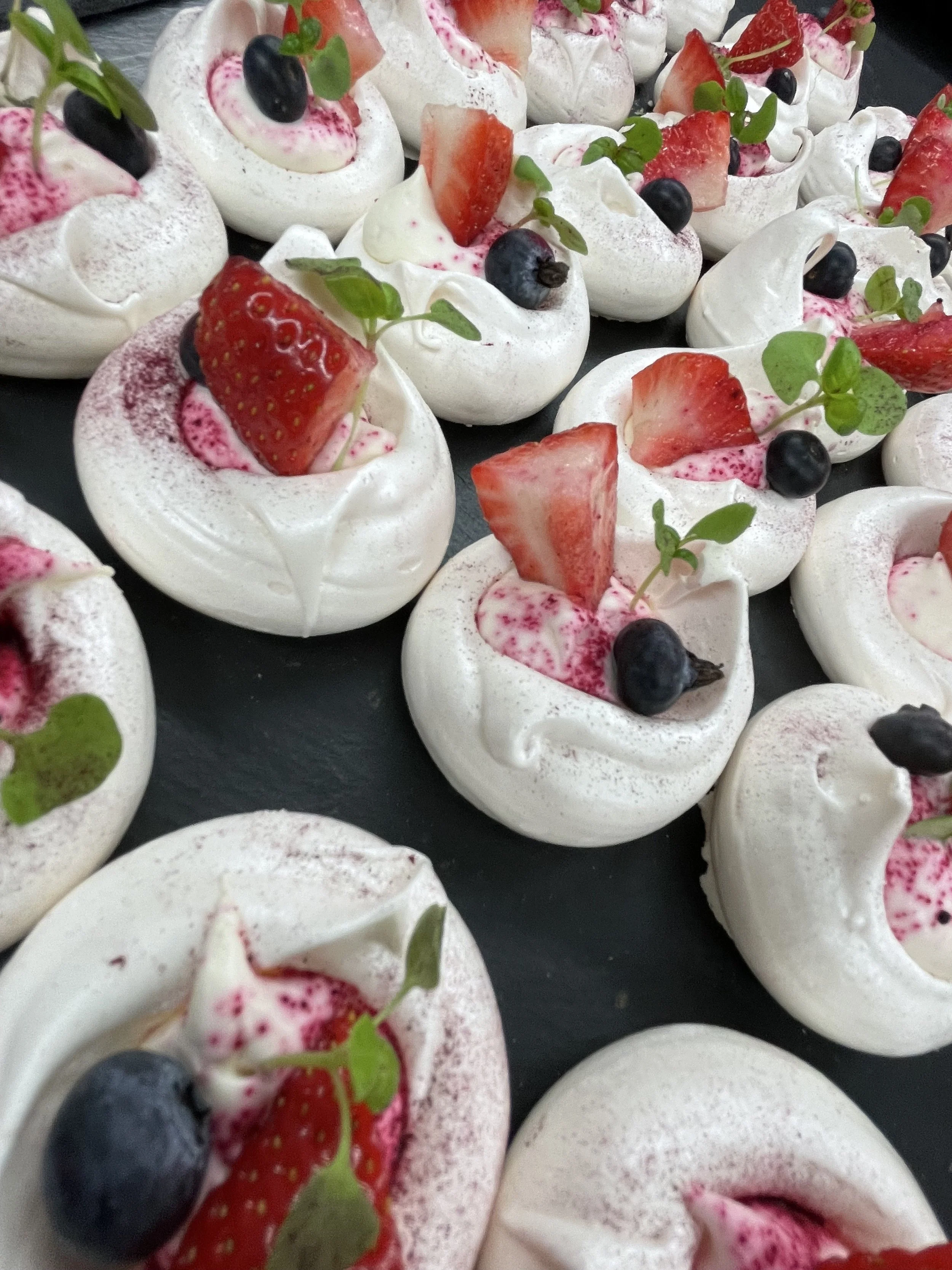 Mini pavlovas topped with strawberries, blueberries, microgreens, and pink powdered sugar.