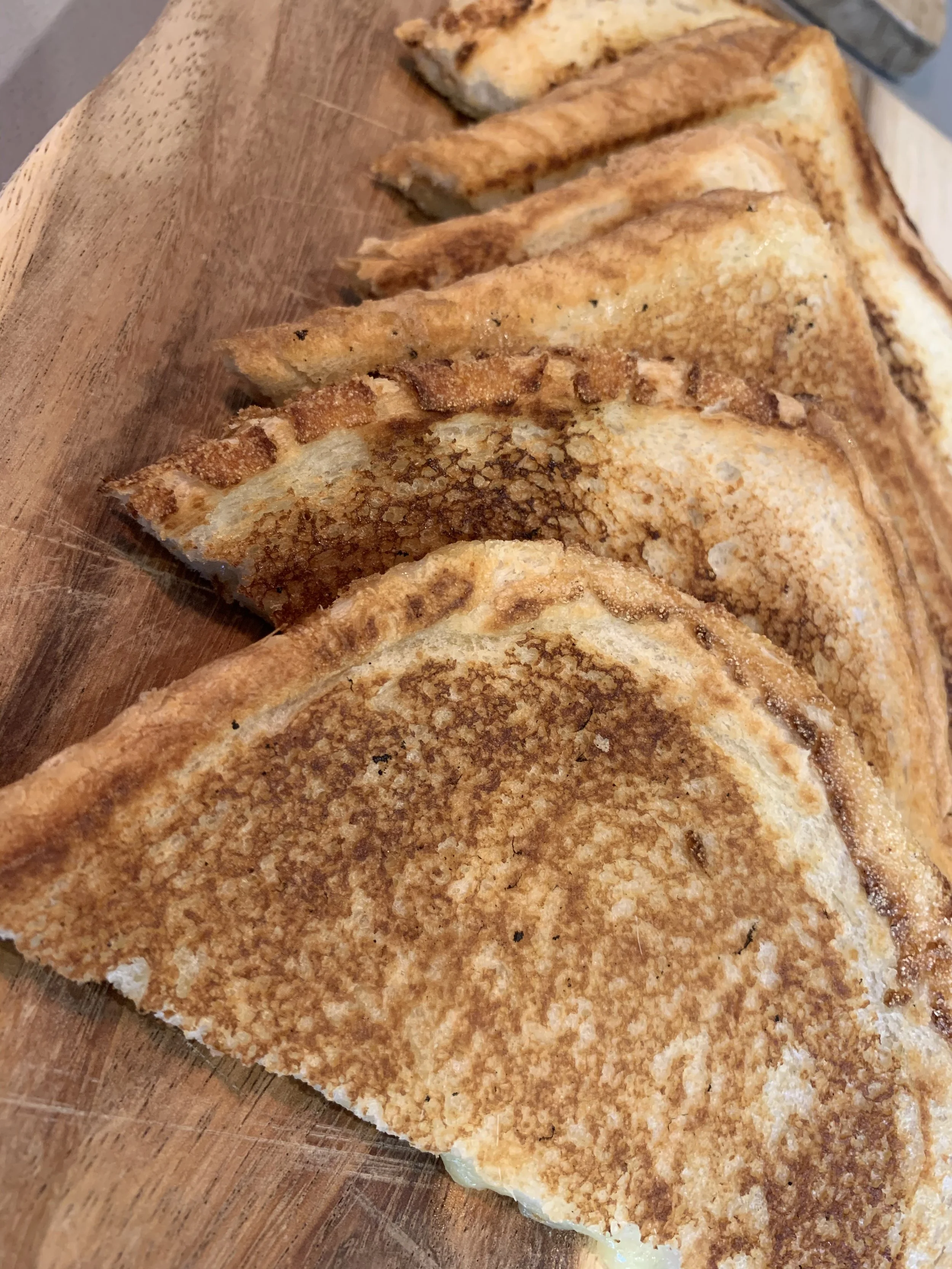 A wooden cutting board with several golden-brown toasted grilled cheese sandwiches, cut into triangles.