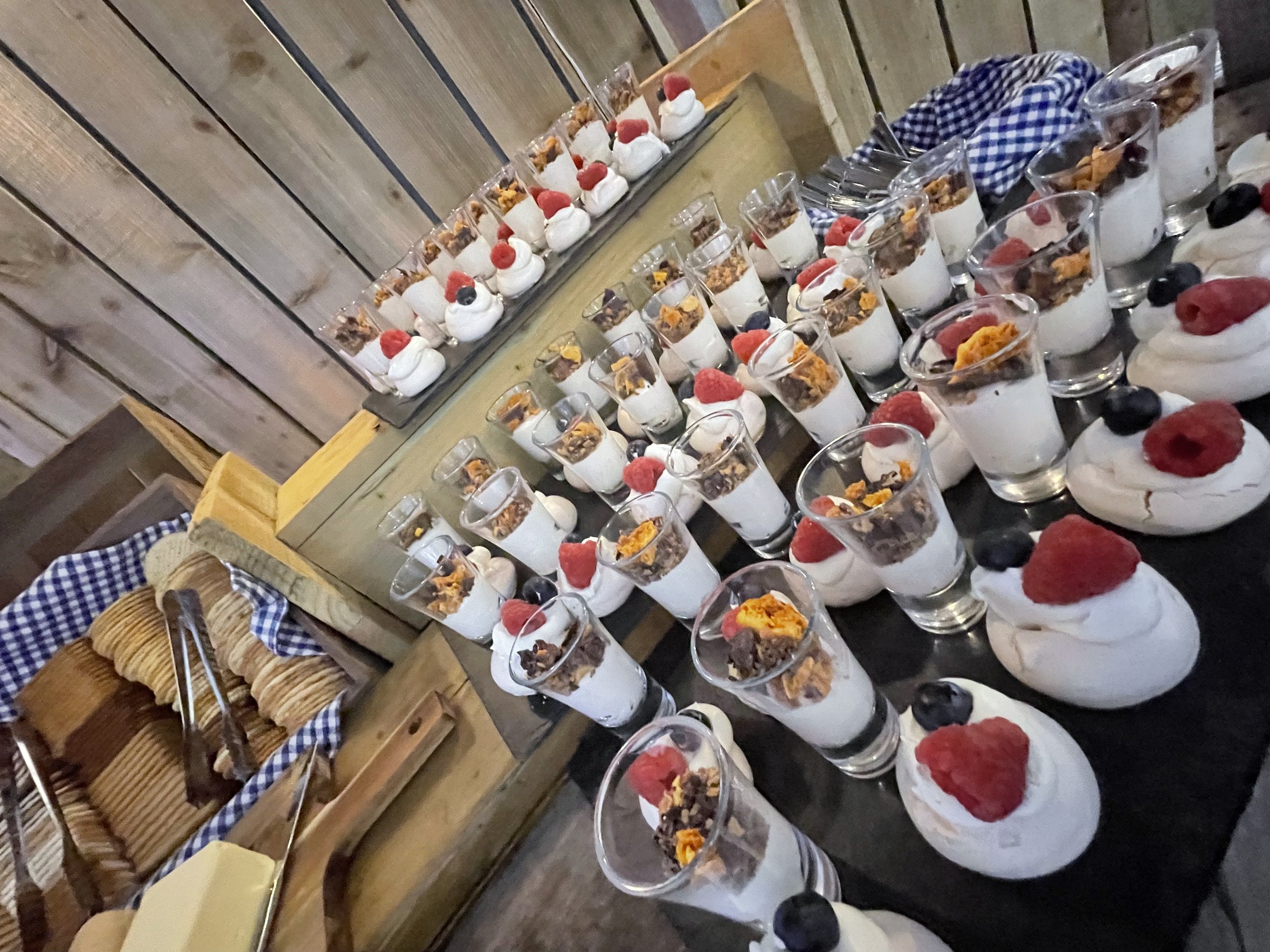 Dessert table featuring individual servings of parfaits in glasses topped with berries and garnishes, alongside a platter of sliced cookies.
