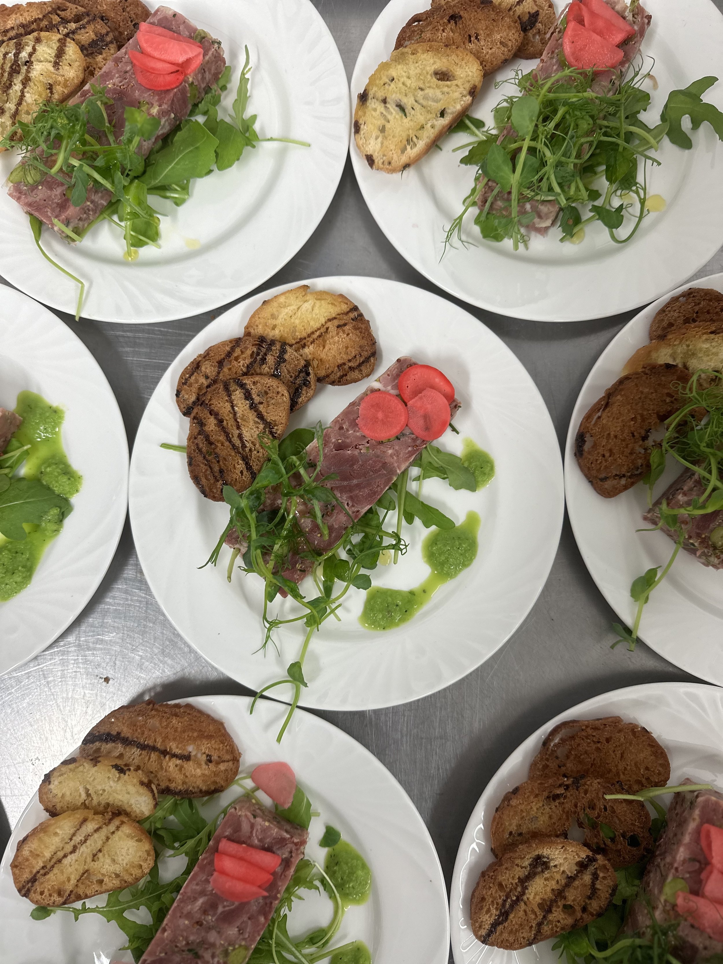 Plated appetizers with seared meat terrine garnished with microgreens and sliced radishes, served with toasted bread and drizzled green sauce.